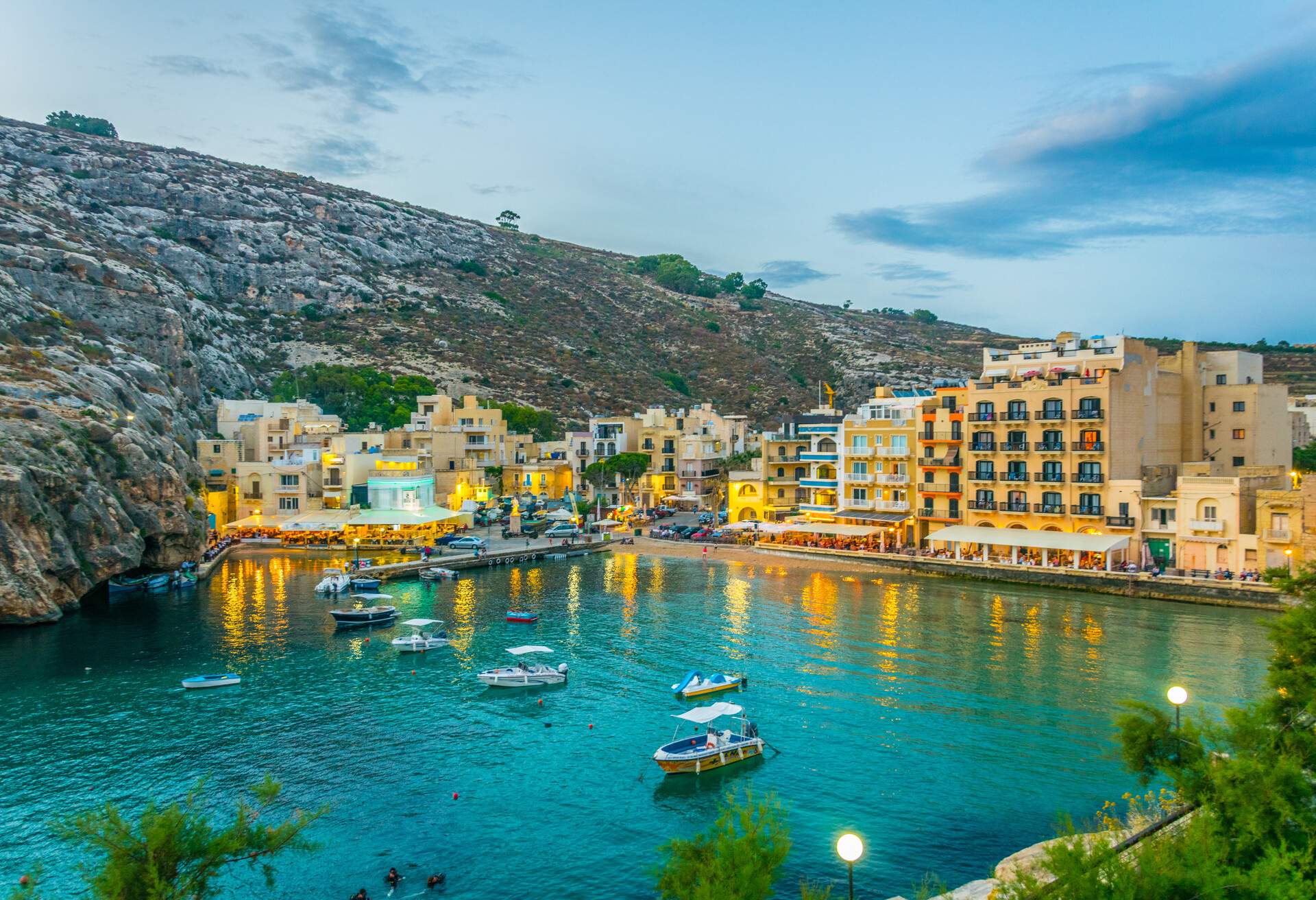 A stunning harbour town with illuminated buildings along the waterfront and yachts floating in the sea.