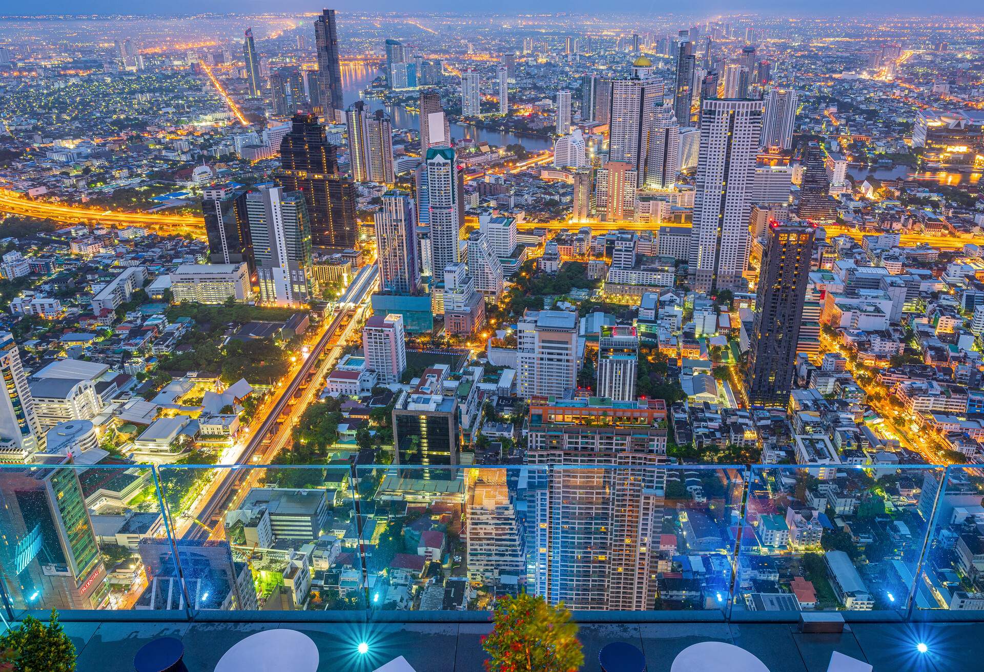 Brightly lit urban scenery with skyscrapers seen from a rooftop bar at dusk.