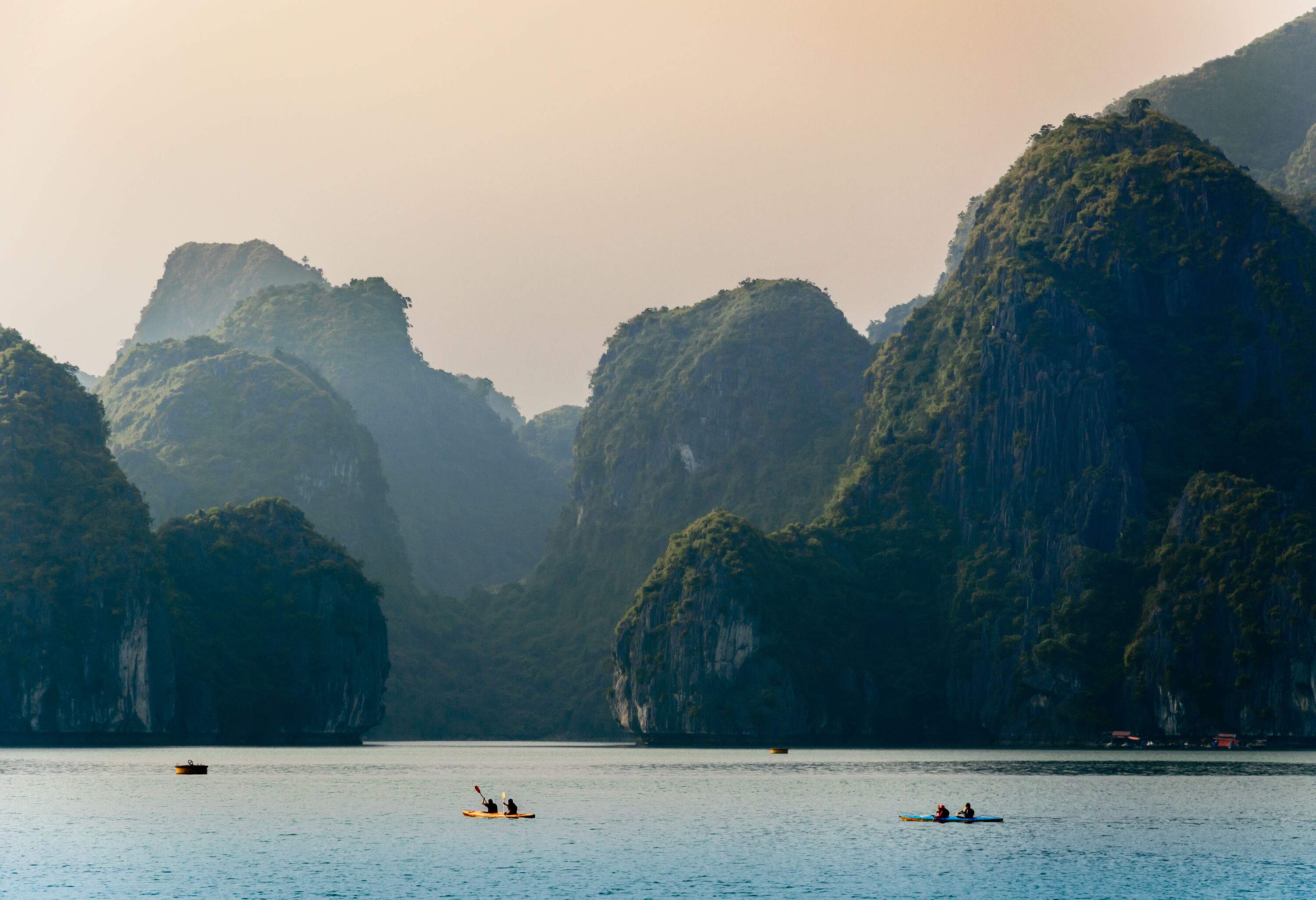 A serene sea with people kayaking amidst picturesque limestone karsts, resembling a scene from a fairy tale.