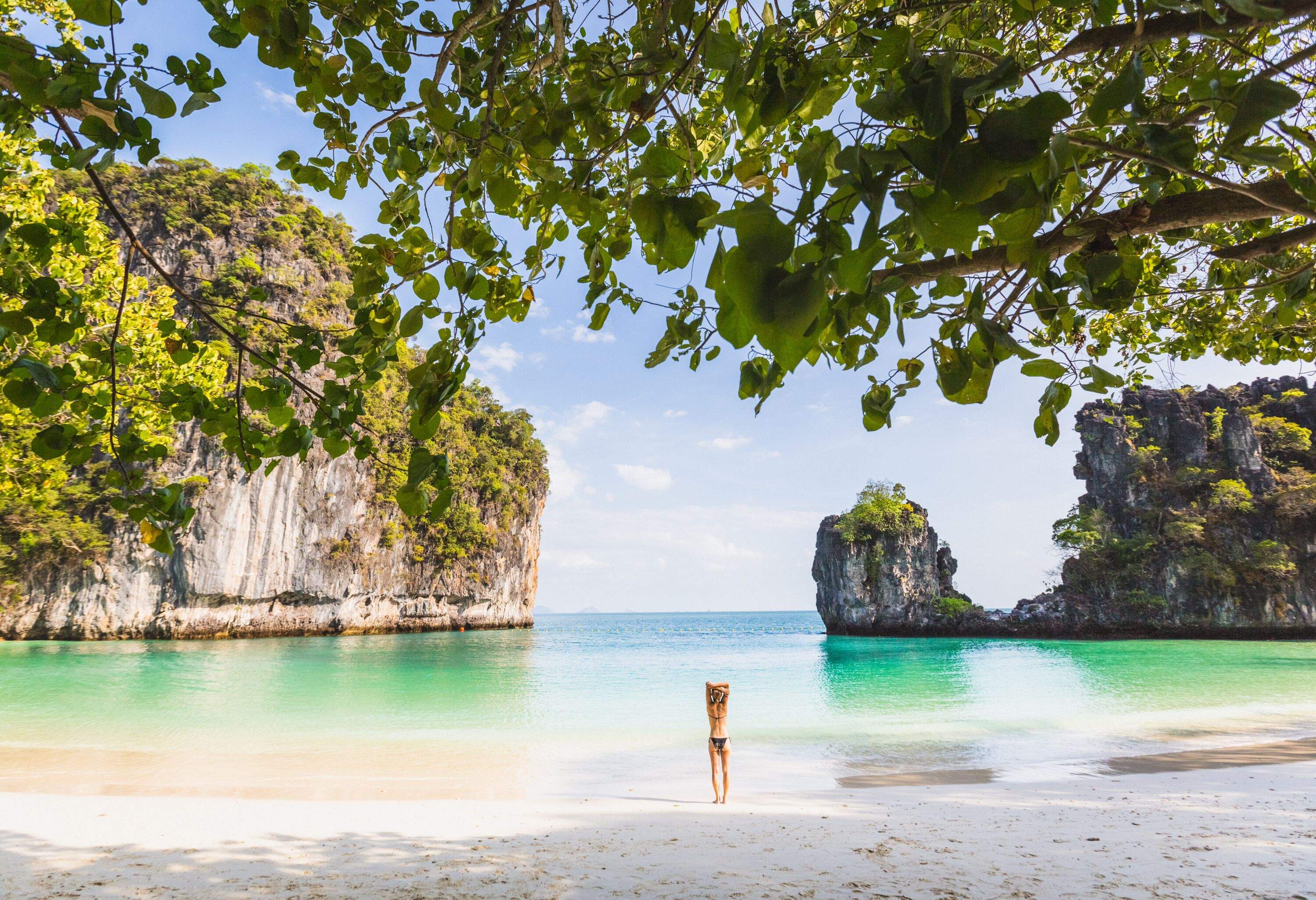 A woman basks in the beauty of a white sand beach on a picturesque island, with stunning rock formations nearby adding to the natural splendour.