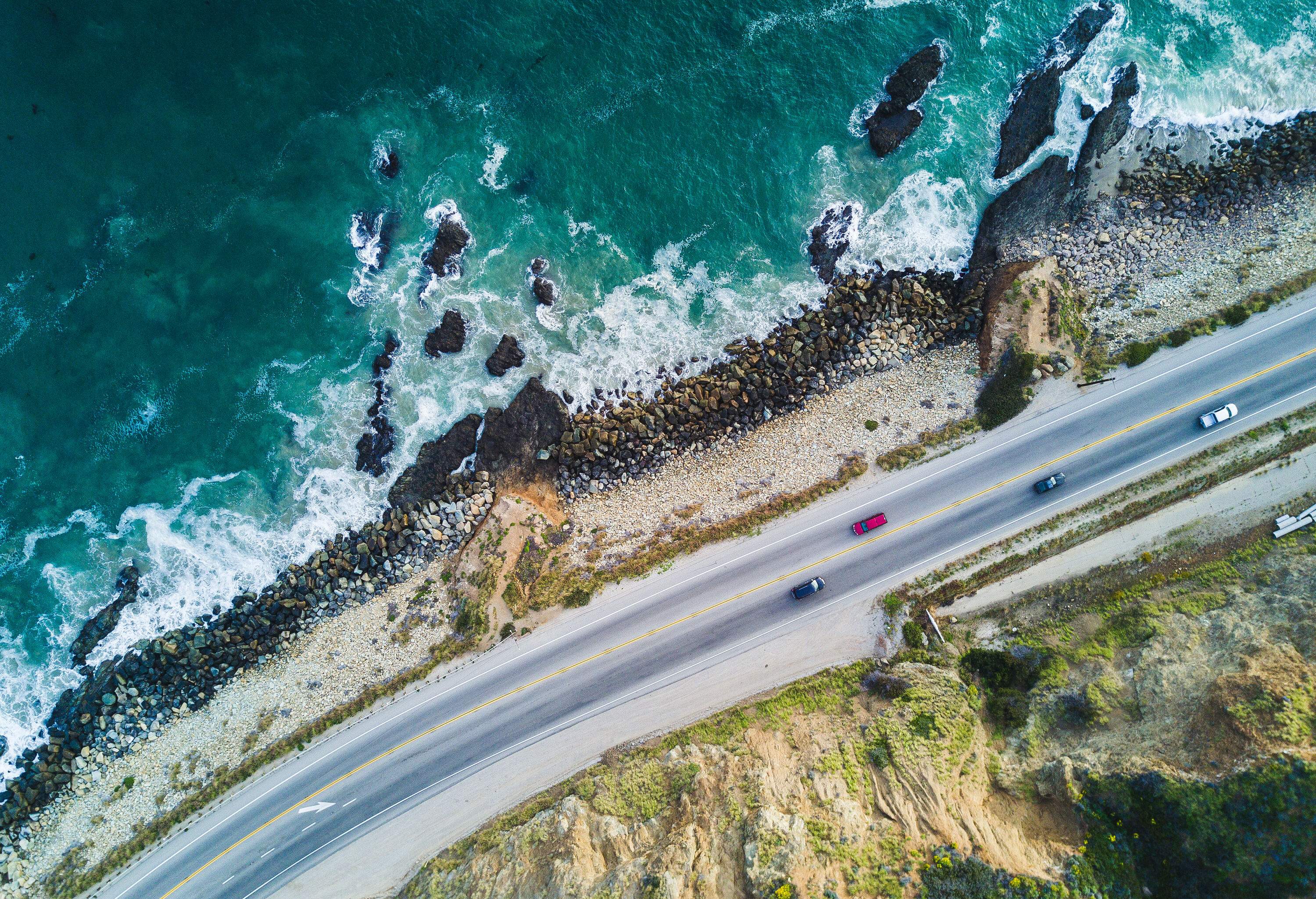 Aerial view of a picturesque road by the rocky shore of the wavy turquoise sea.