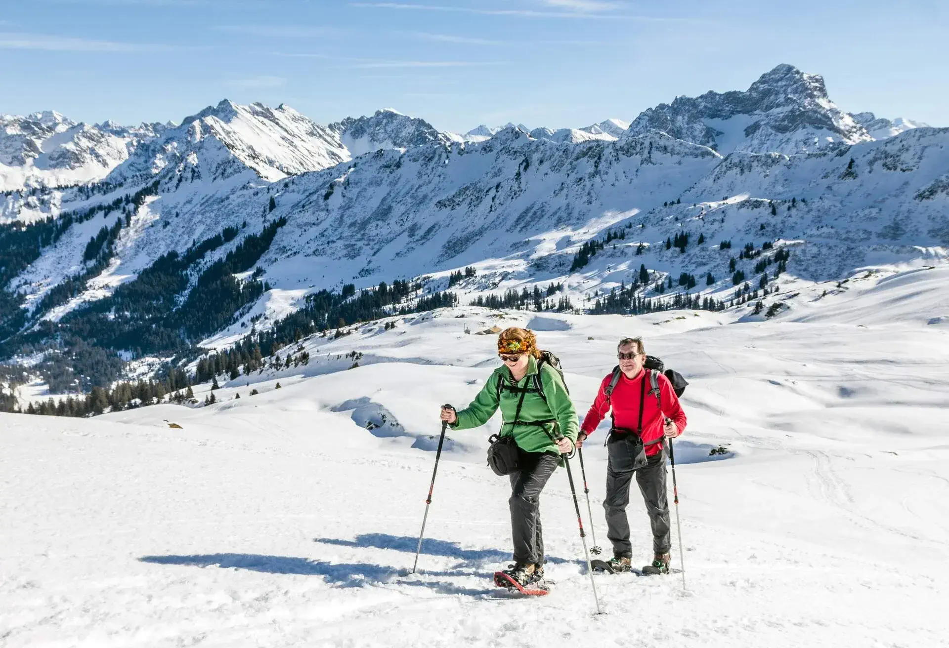 A couple of hikers traversing a snowy landscape with icy mountains in the background.
