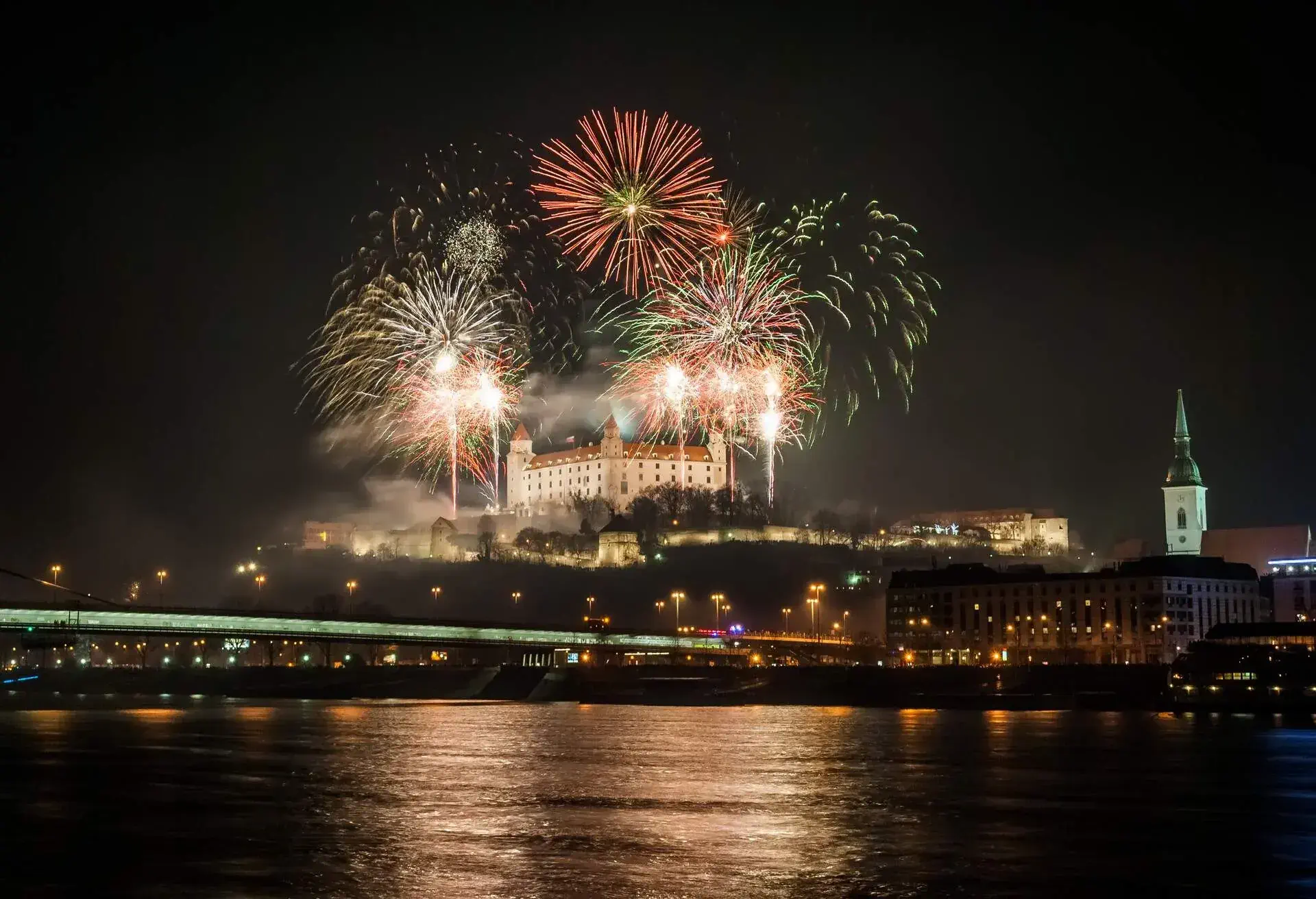 Bright fireworks across the river offer a magnificent show against the urban backdrop as they illuminate Bratislava Castle's outline.