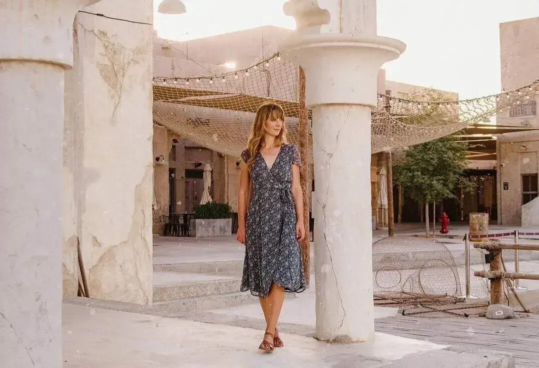 Woman in a dress walking through Dubai with the columns of an old building and fairy lights in the background