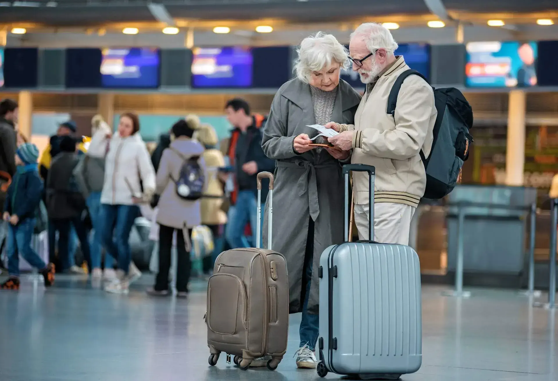 Seniors standing at the airport with their suitcases and reading something