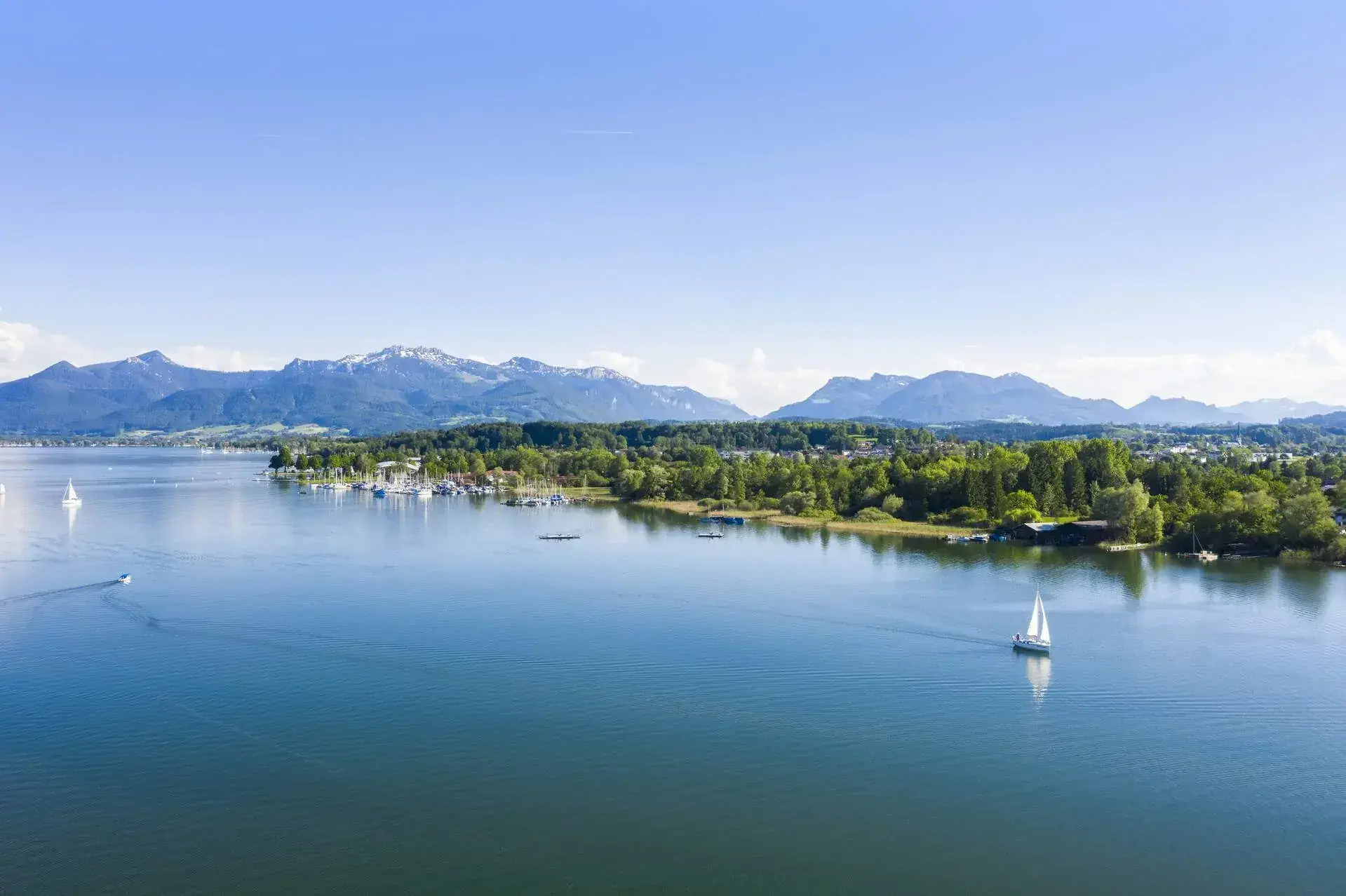 A scenic lake with coasts lined with trees and distant mountains.