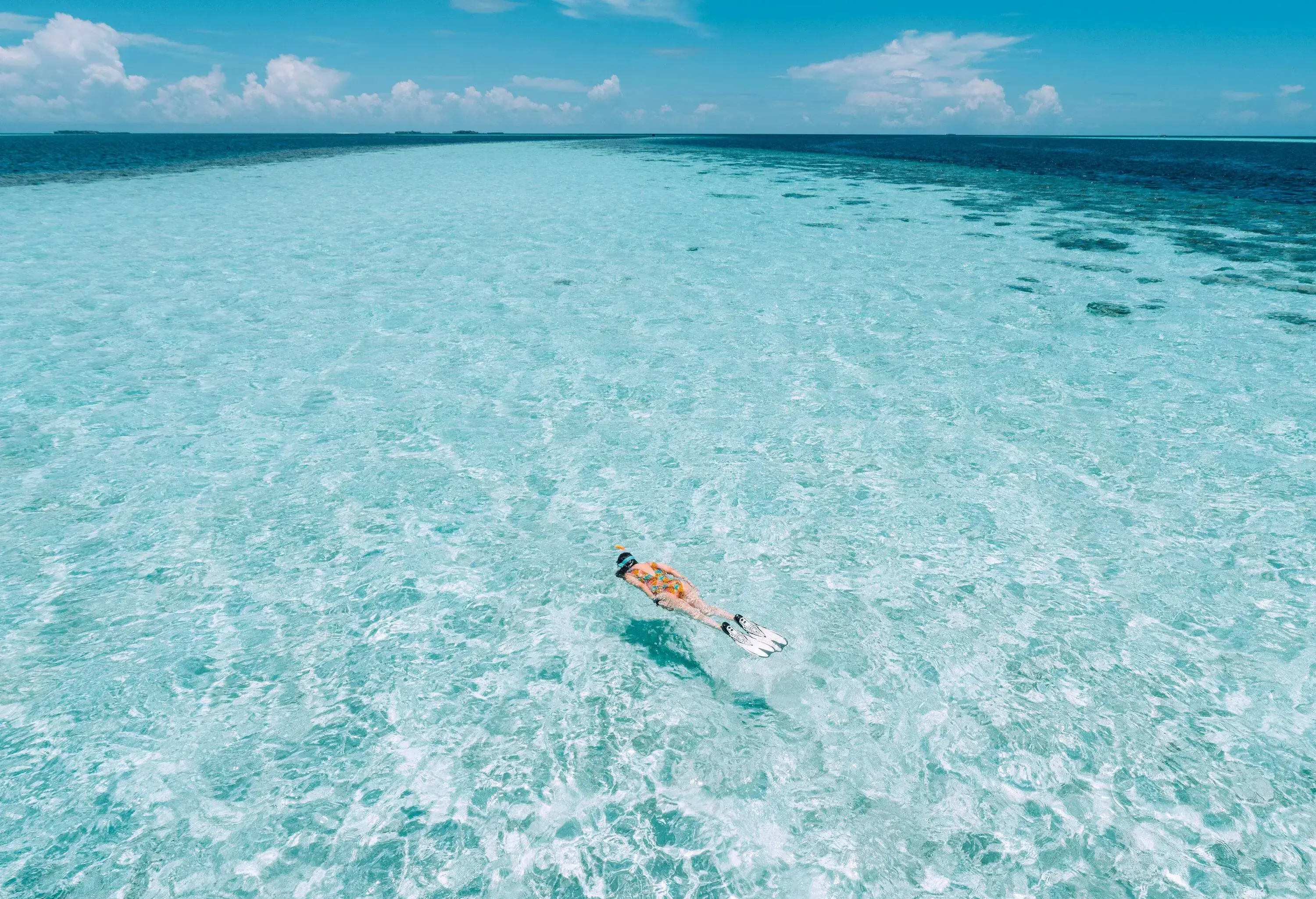 A woman in a bathing suit snorkels across the crystal-clear turquoise waters.