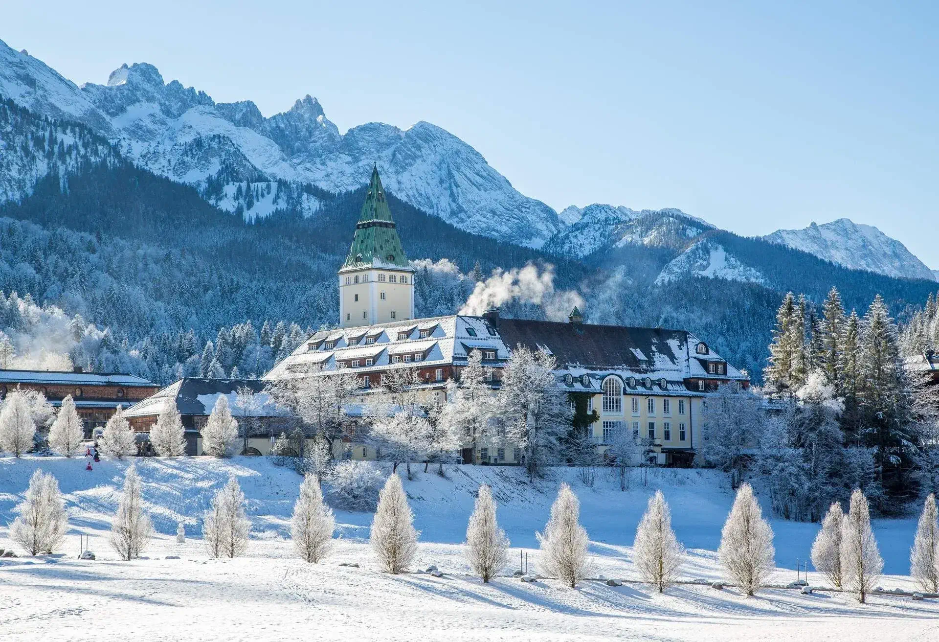 A traditional German castle surrouned by trees at the bottom of a mountain range, landscape covered in snow on a sunny day
