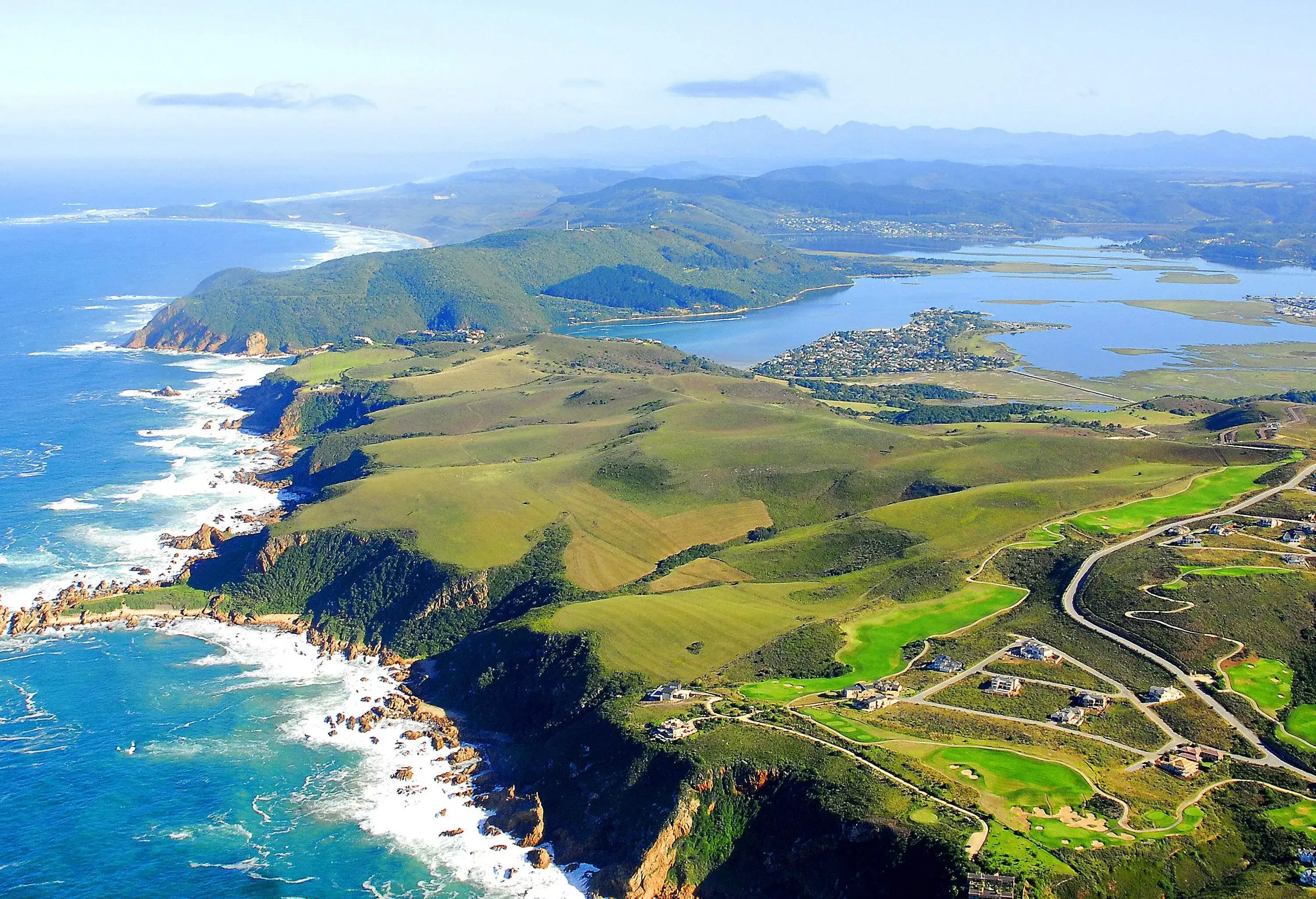 A cluster of homes and its surrounding roads near a coastal cliff with views of a big river that flows into the ocean.