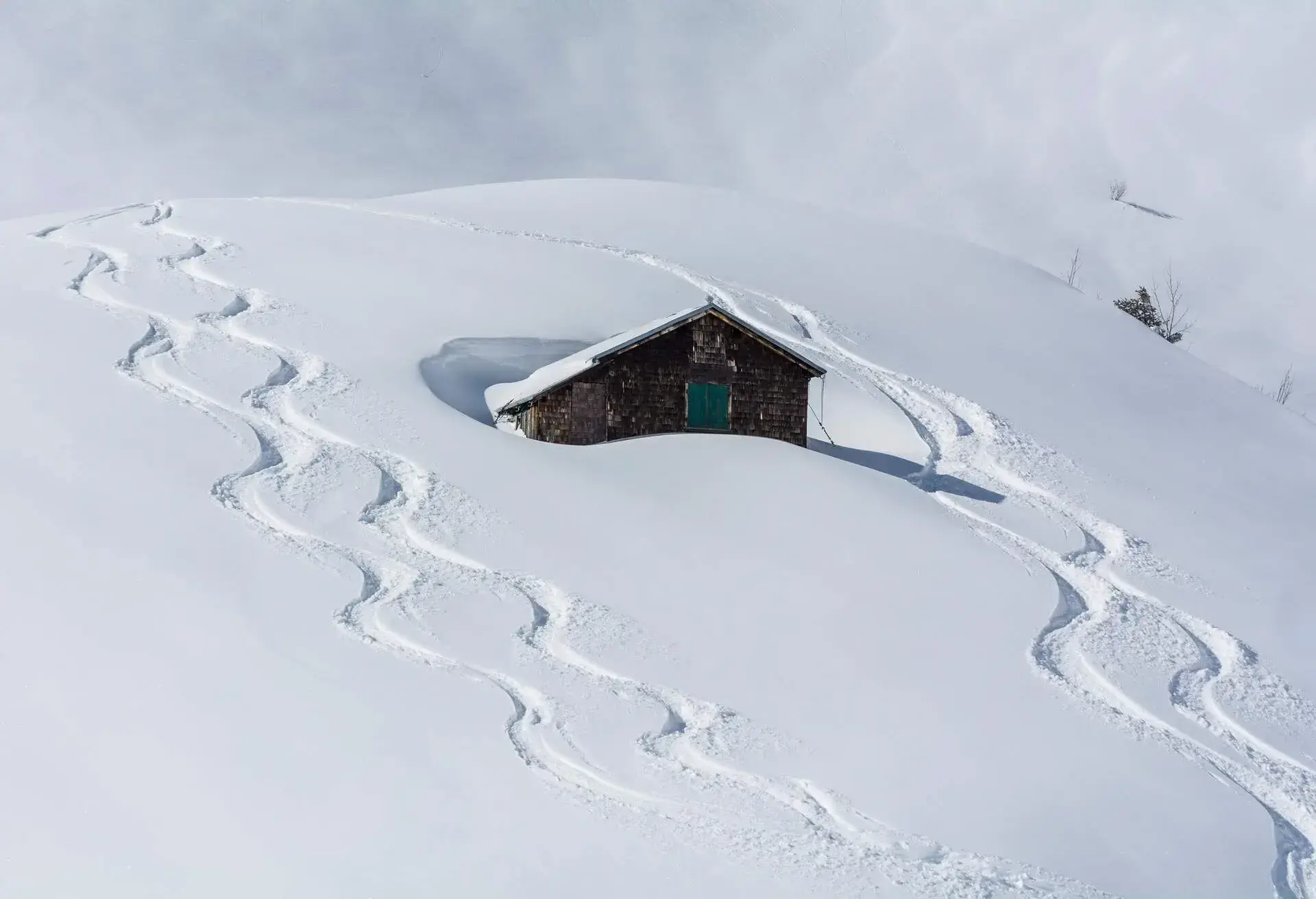 A hillside cabin buried in deep snow with ski tracks.