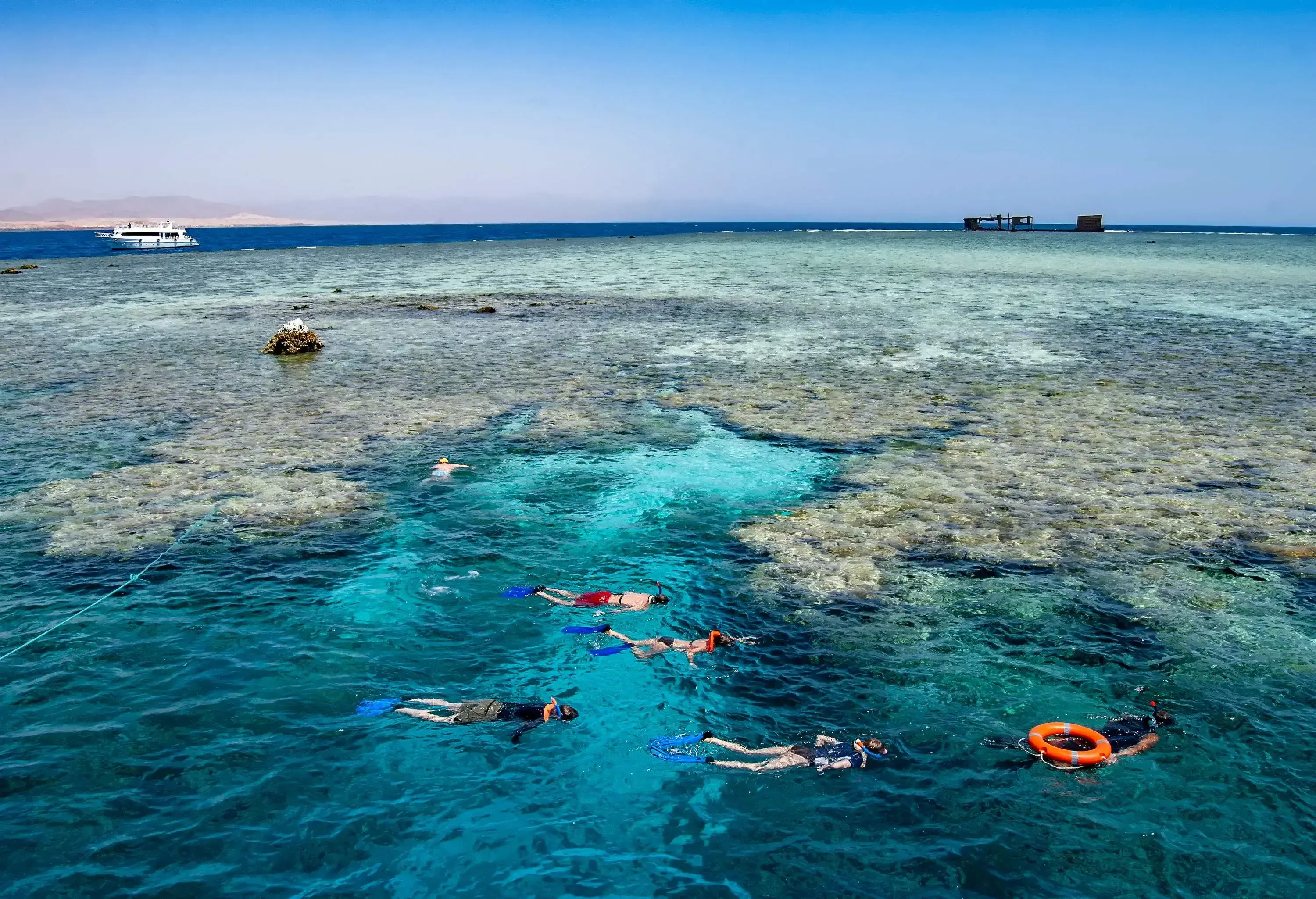 A group of snorkelers swim across the crystal-clear waters with coral reefs visible underwater.
