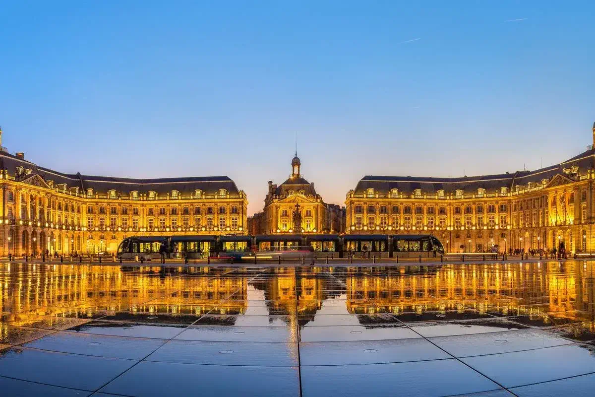 Panorama of illuminated Place de la Bourse with tram and water mirror fountain in Bordeaux 