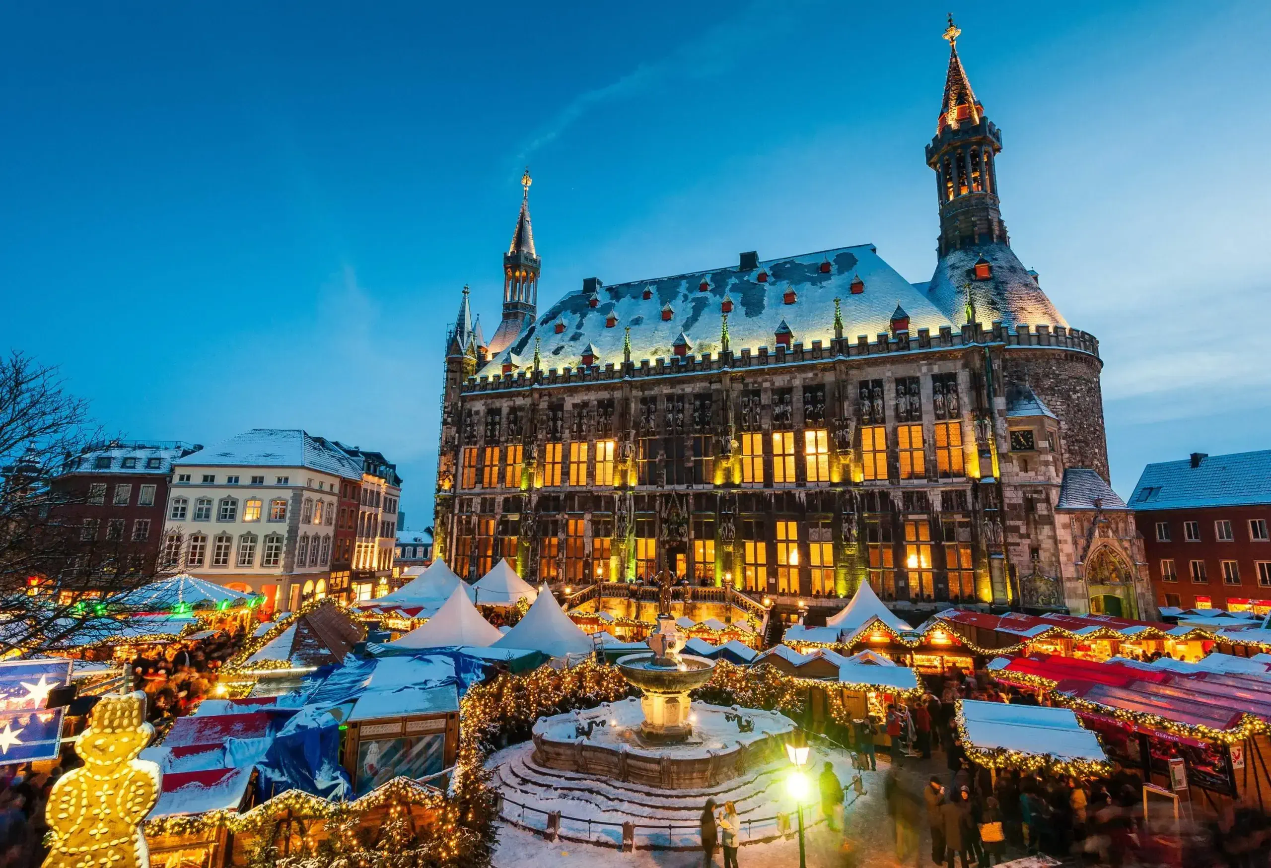 Market stalls decked out with holiday decor are set off by a massive brick building with towers at either end.