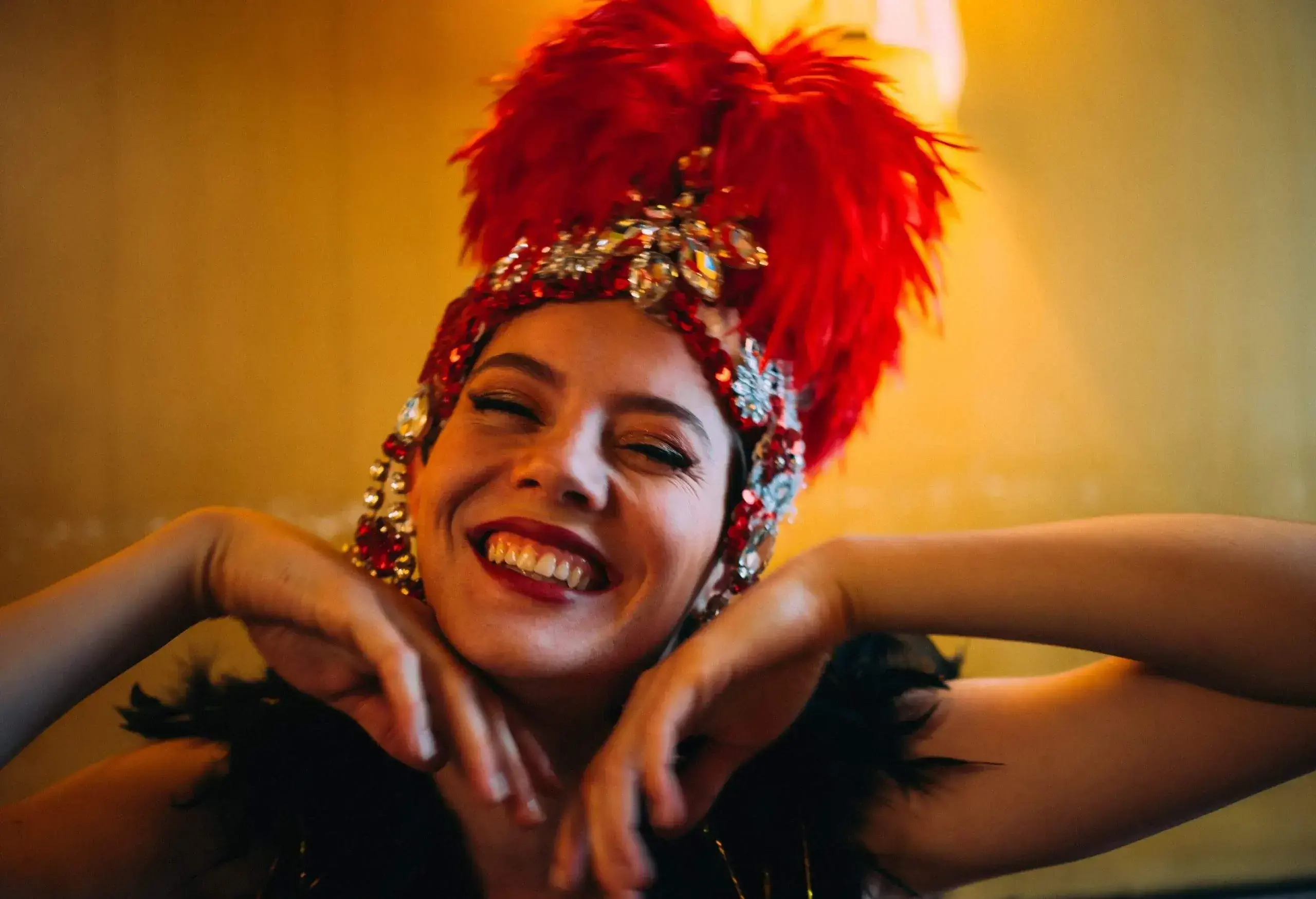 A person with a red feathered headpiece and black feathered top smiles happily.