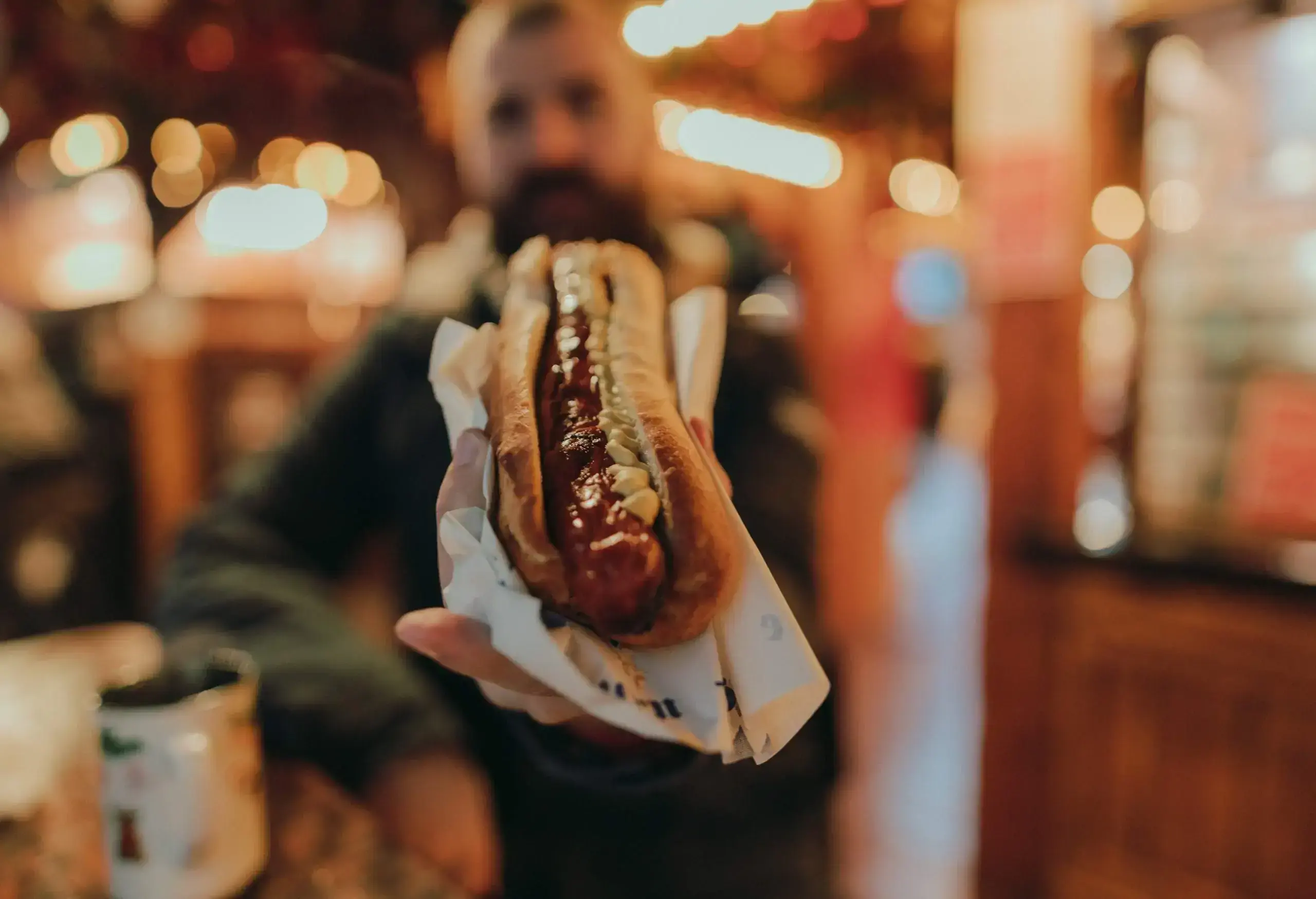 A man shows a bread bun with hotdog and mayonnaise.