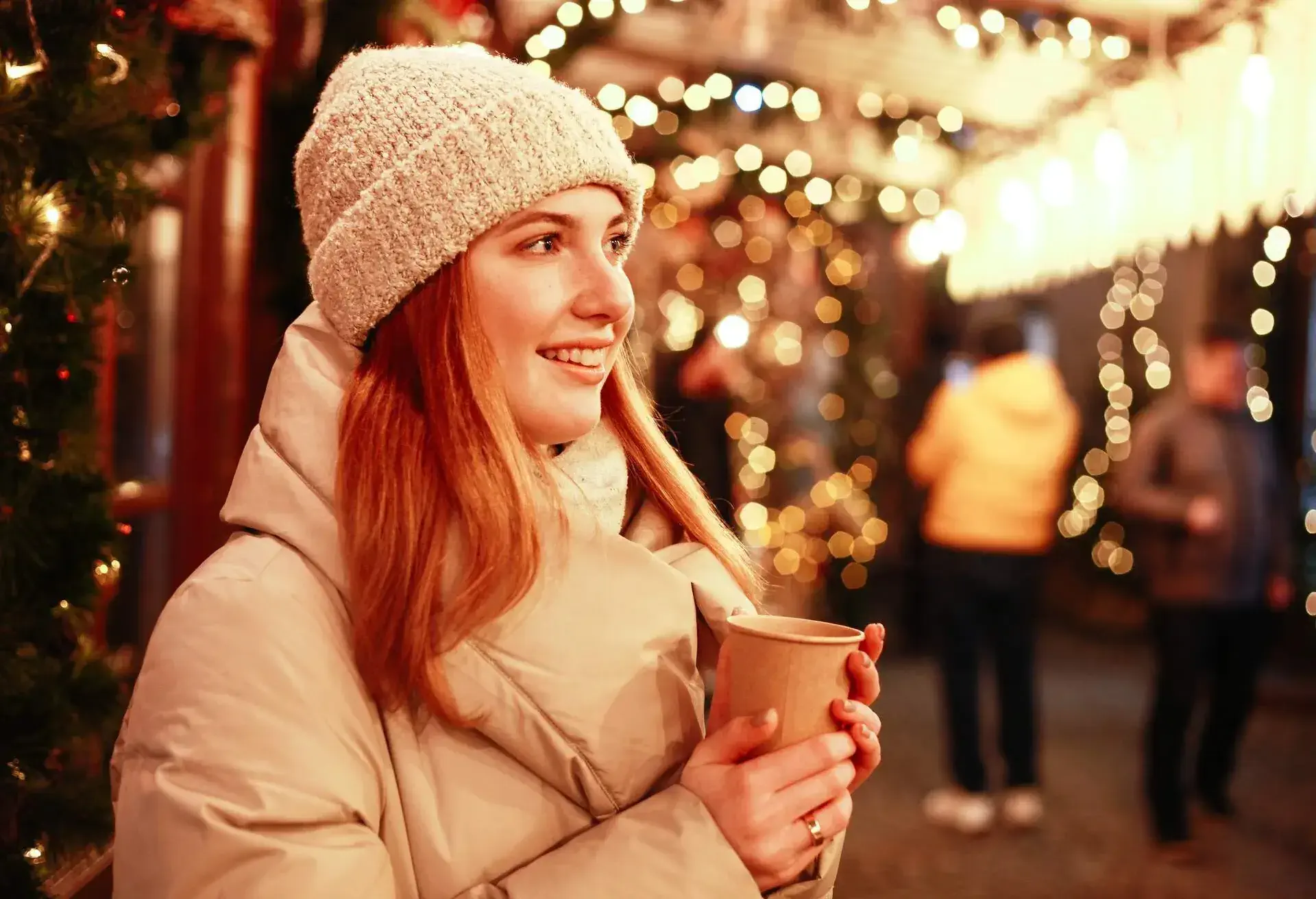 Woman wearing winter jacket and wool hat smiling at Christmas market