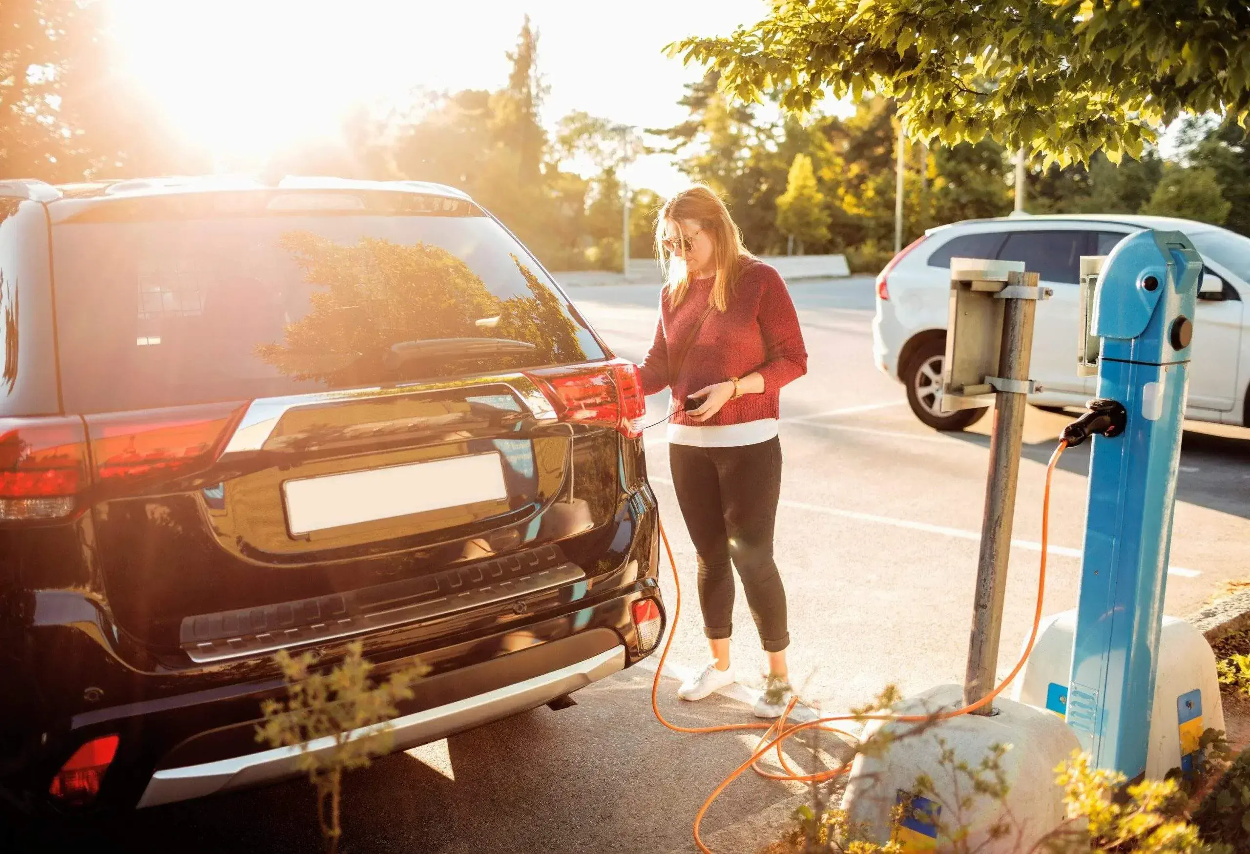 A woman charges an electric car with a cable in a charging station parking lot.