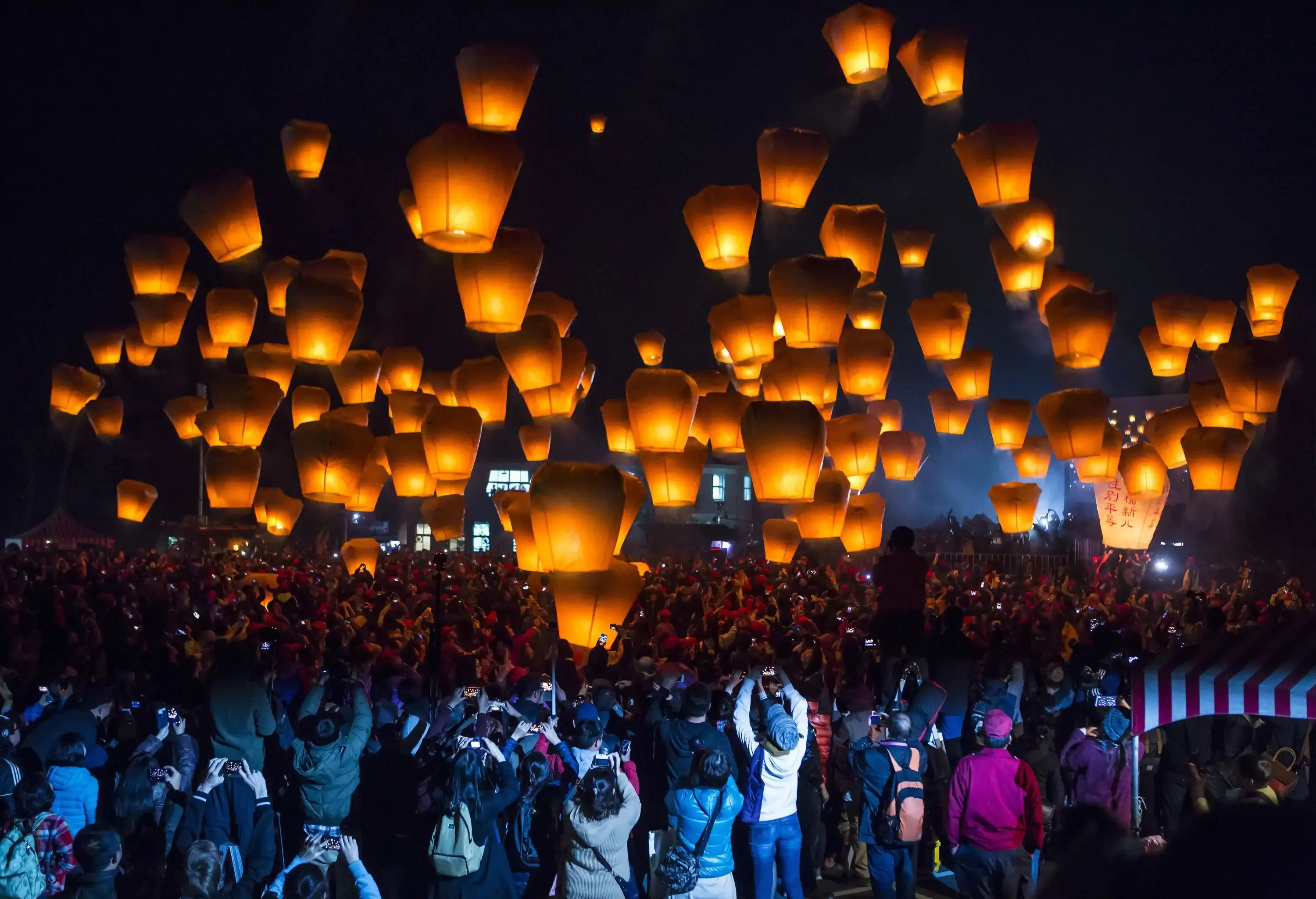 A crowd of people took a picture of the floating lit lanterns during the night.
