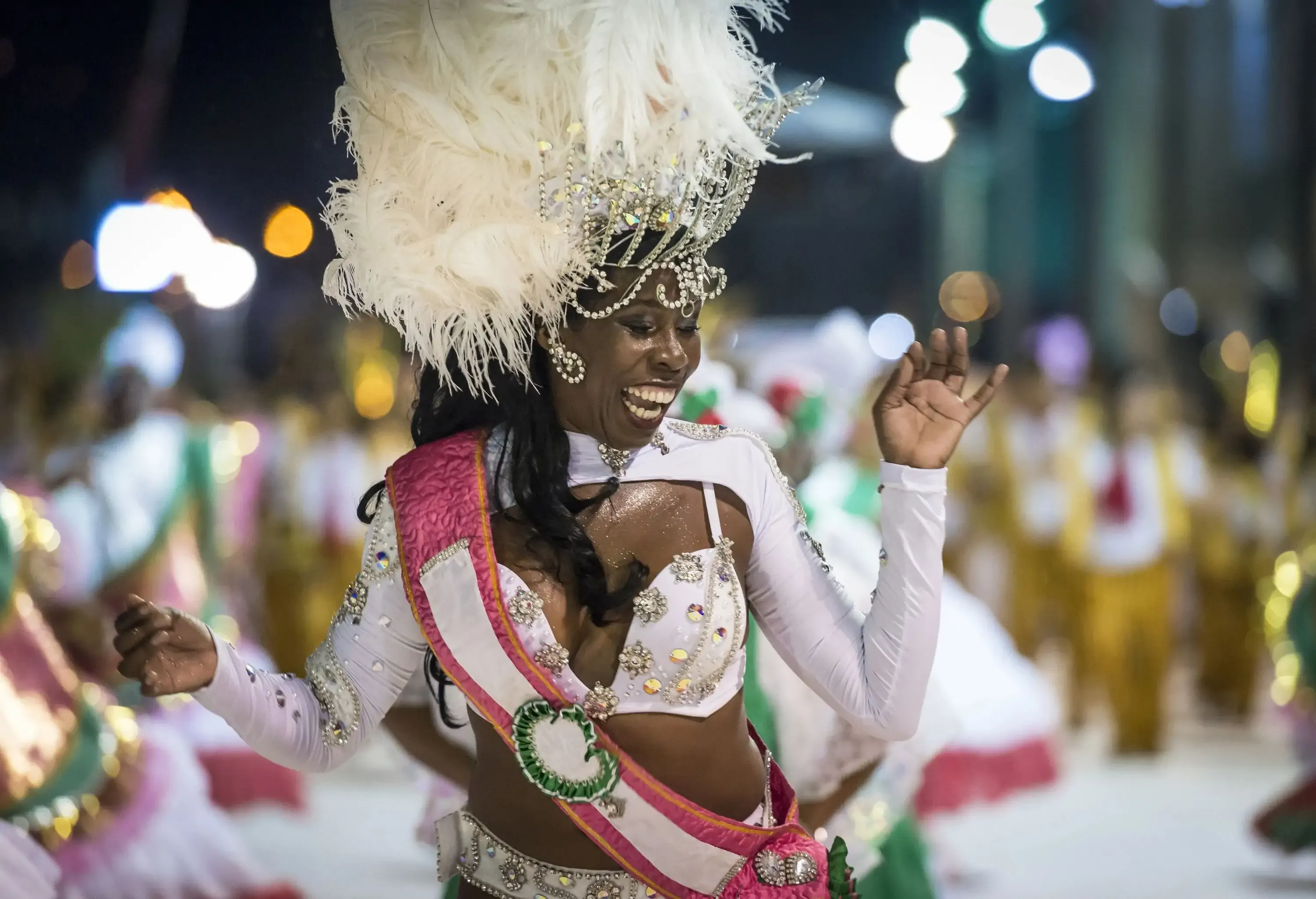 A young and beautiful woman adorned in a dazzling white parade costume, topped with a magnificent feathered headdress, gracefully dances with captivating elegance.