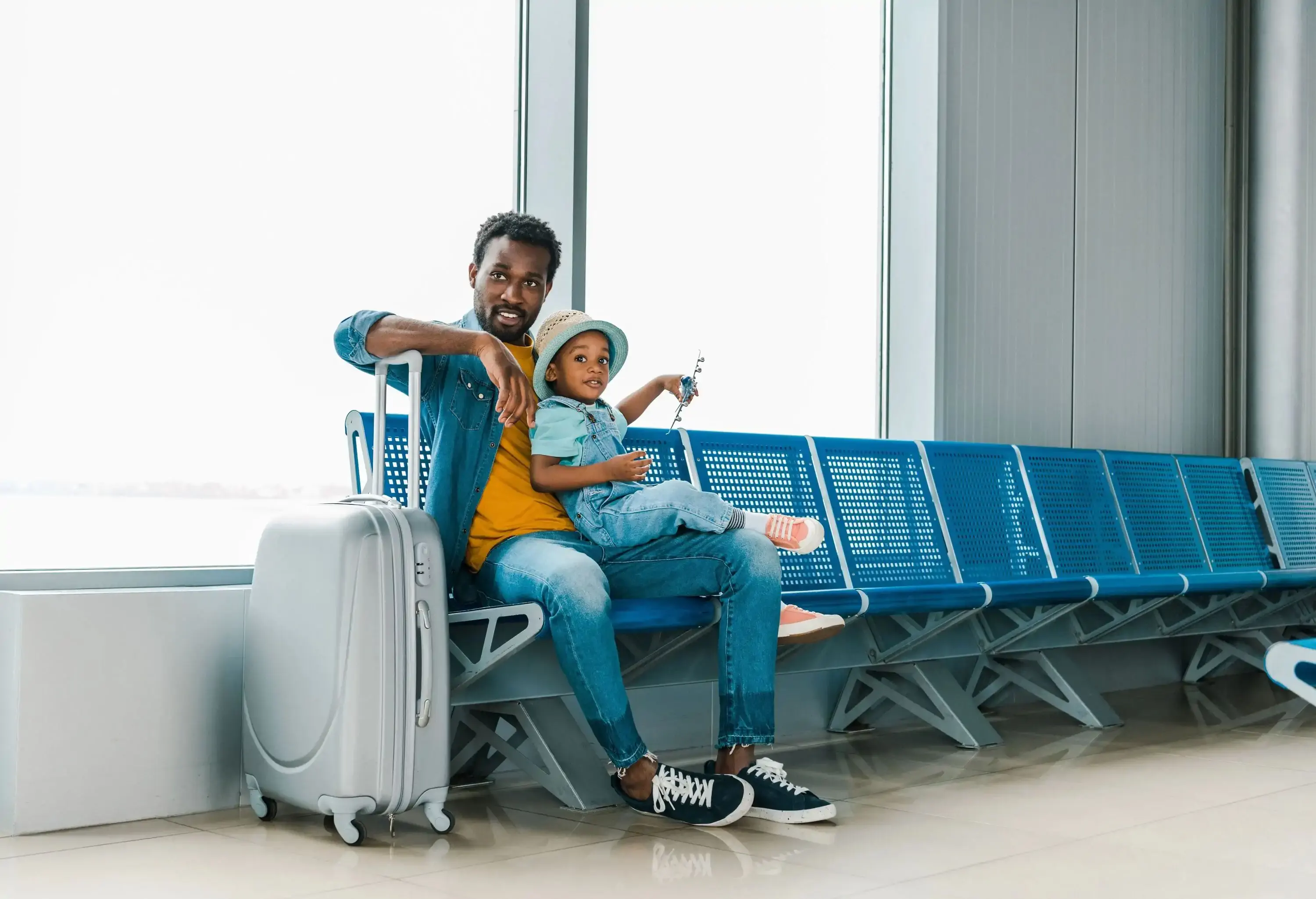 A man sits on a blue bench with a child on his lap next to his luggage.