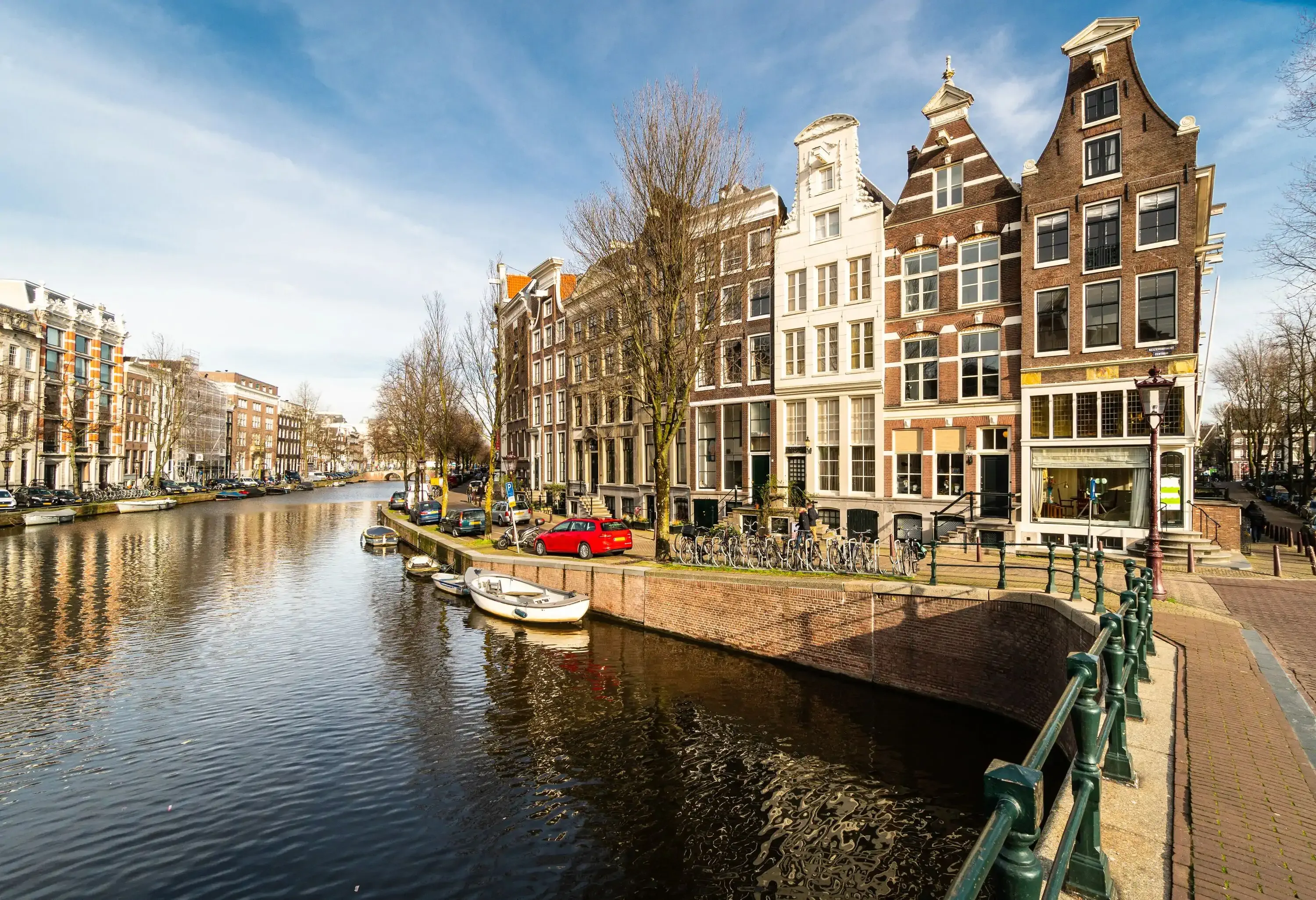 Parked cars and docked boats along a canal next to brown and white adjacent buildings.