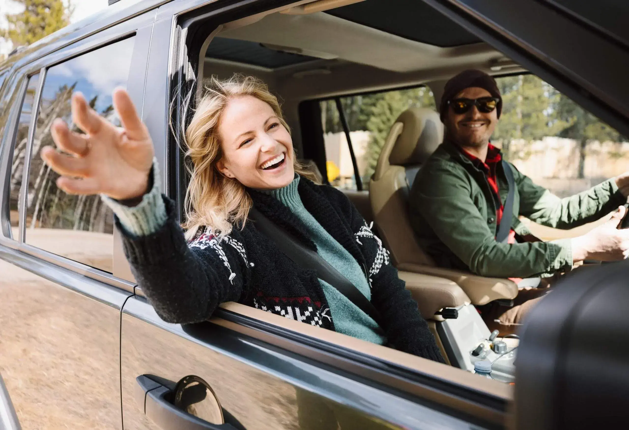 A woman smiling, sitting on the passenger seat, and a man driving the car