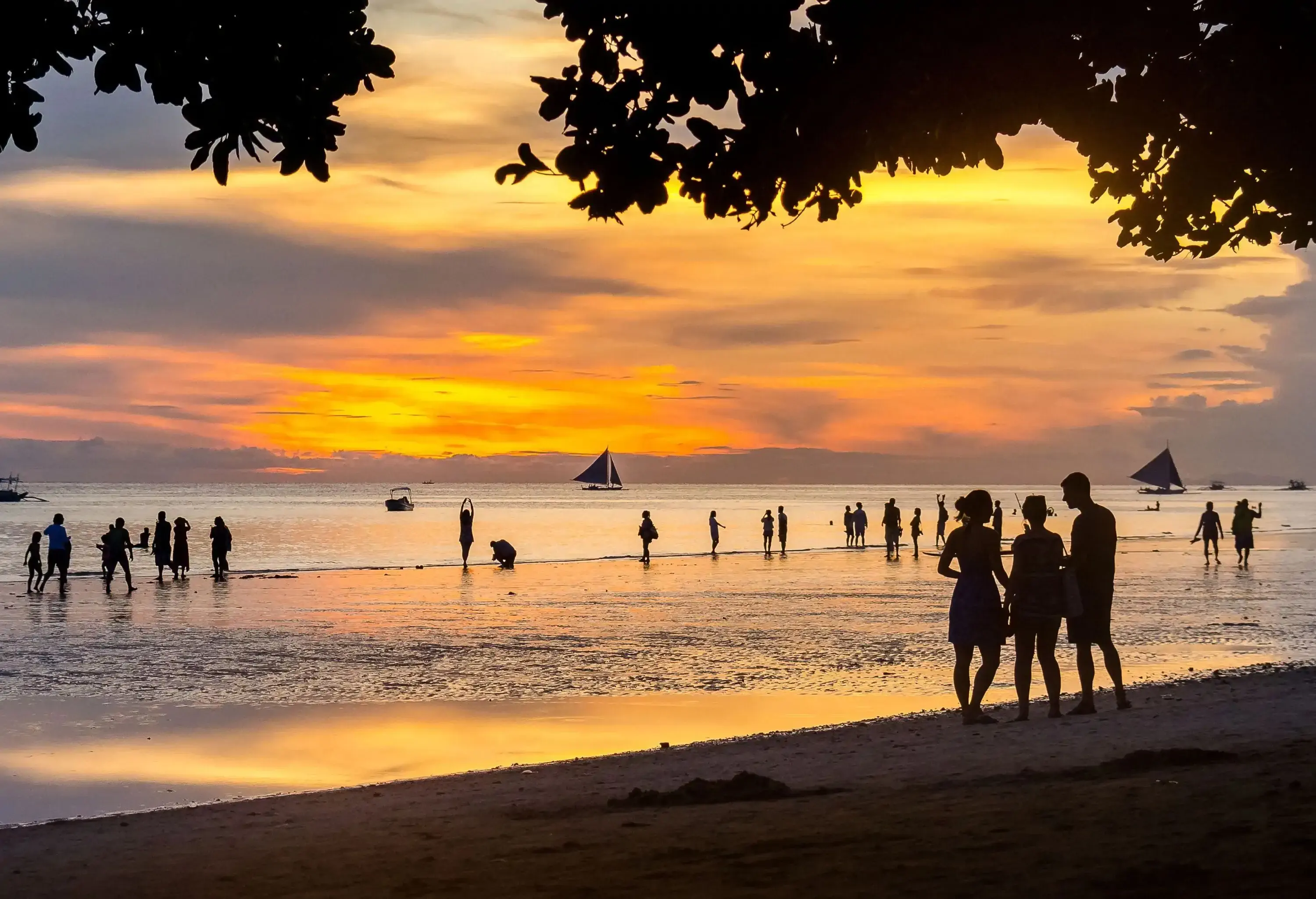 Silhouette of people and boats against the mesmerising backdrop of a Boracay sunset, where the golden hues of the sky and shimmering waters blend to create a breathtaking coastal scene.