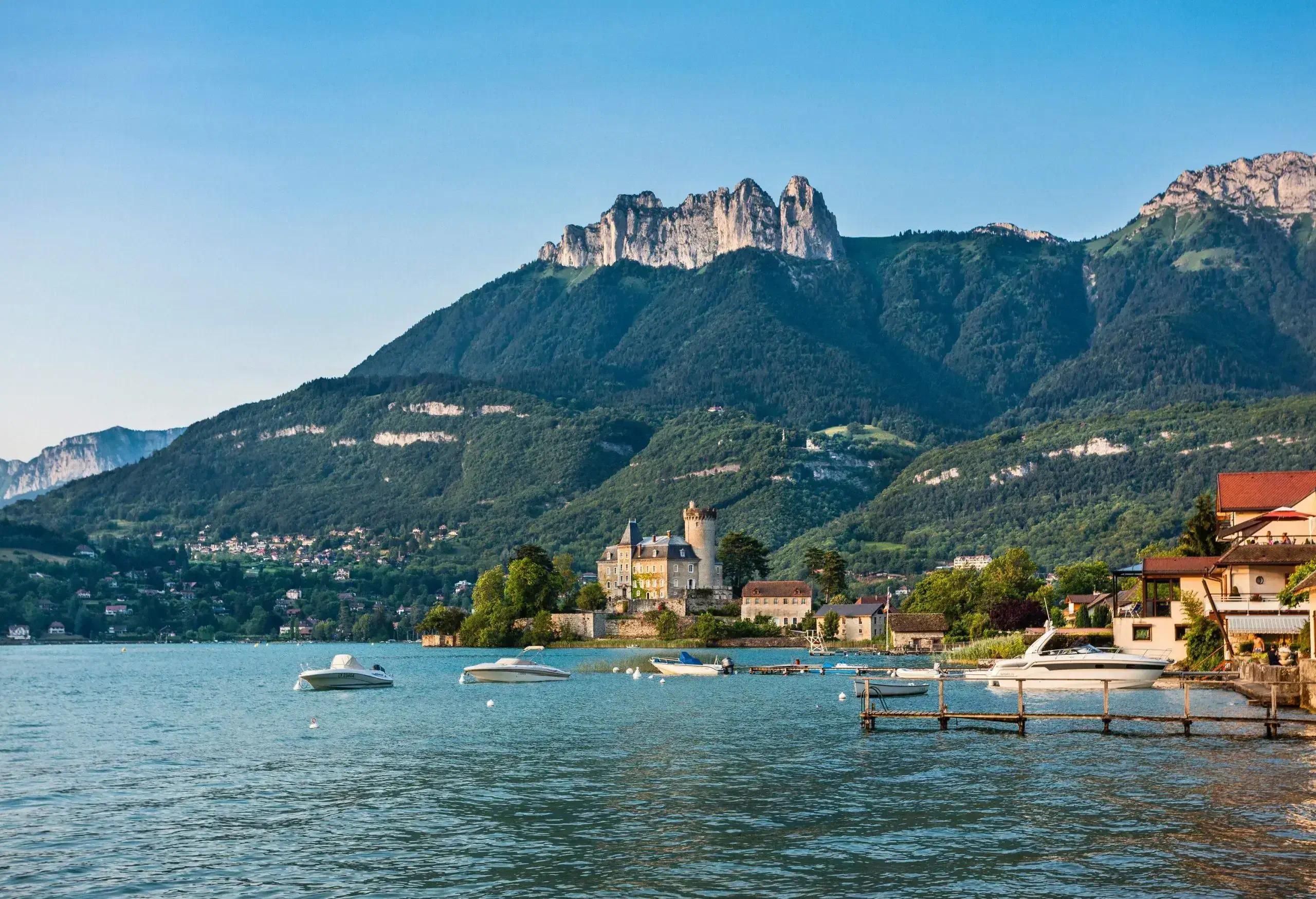 A beautiful village with chateaus beside the lake surrounded by enormous mountains.