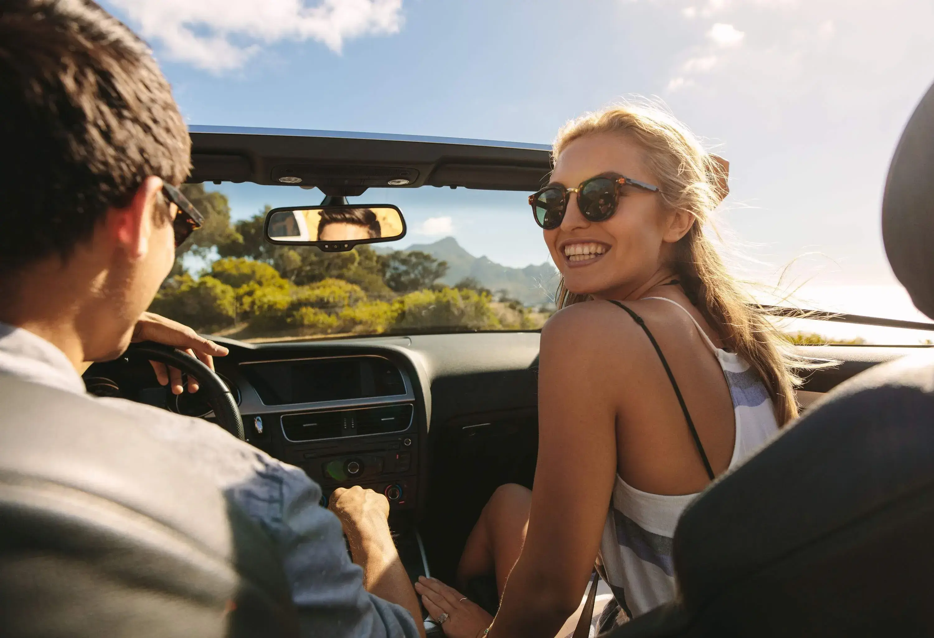 A young lady sitting in the passenger seat as the man takes them on the road in a convertible car.