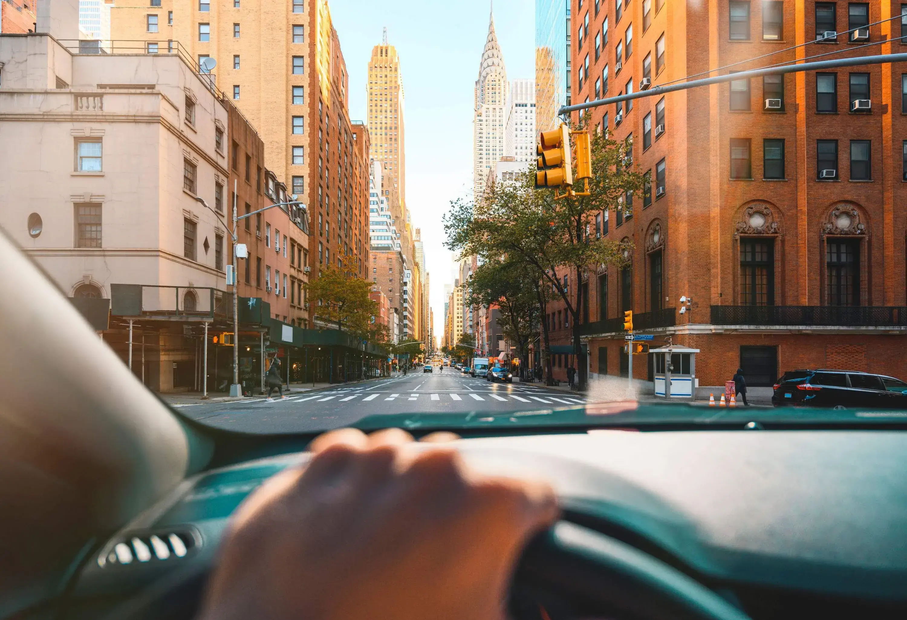 A driver's view inside a car of an intersection and a street lined with tall city buildings.