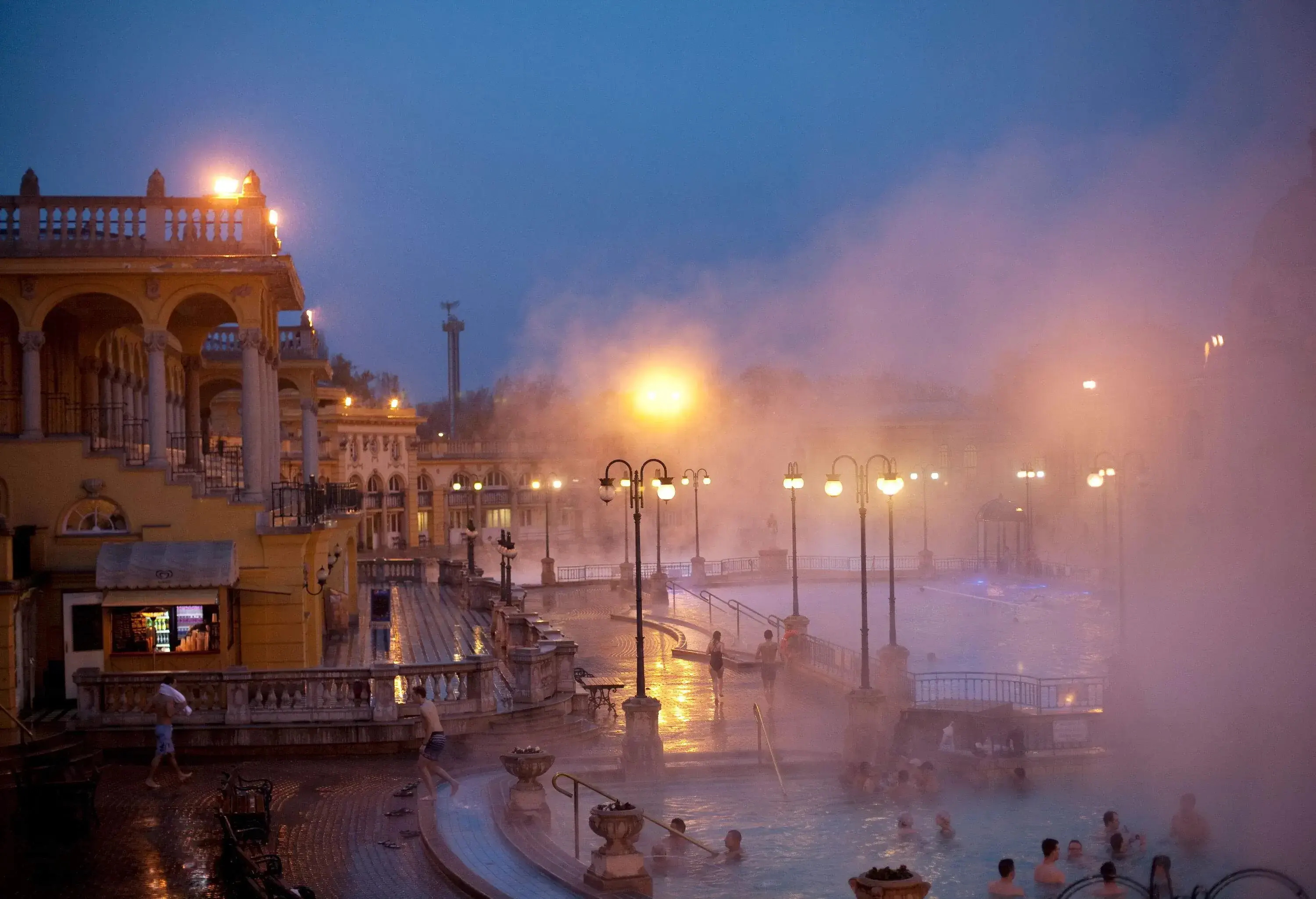 People swim in misty thermal bath pools at dusk.