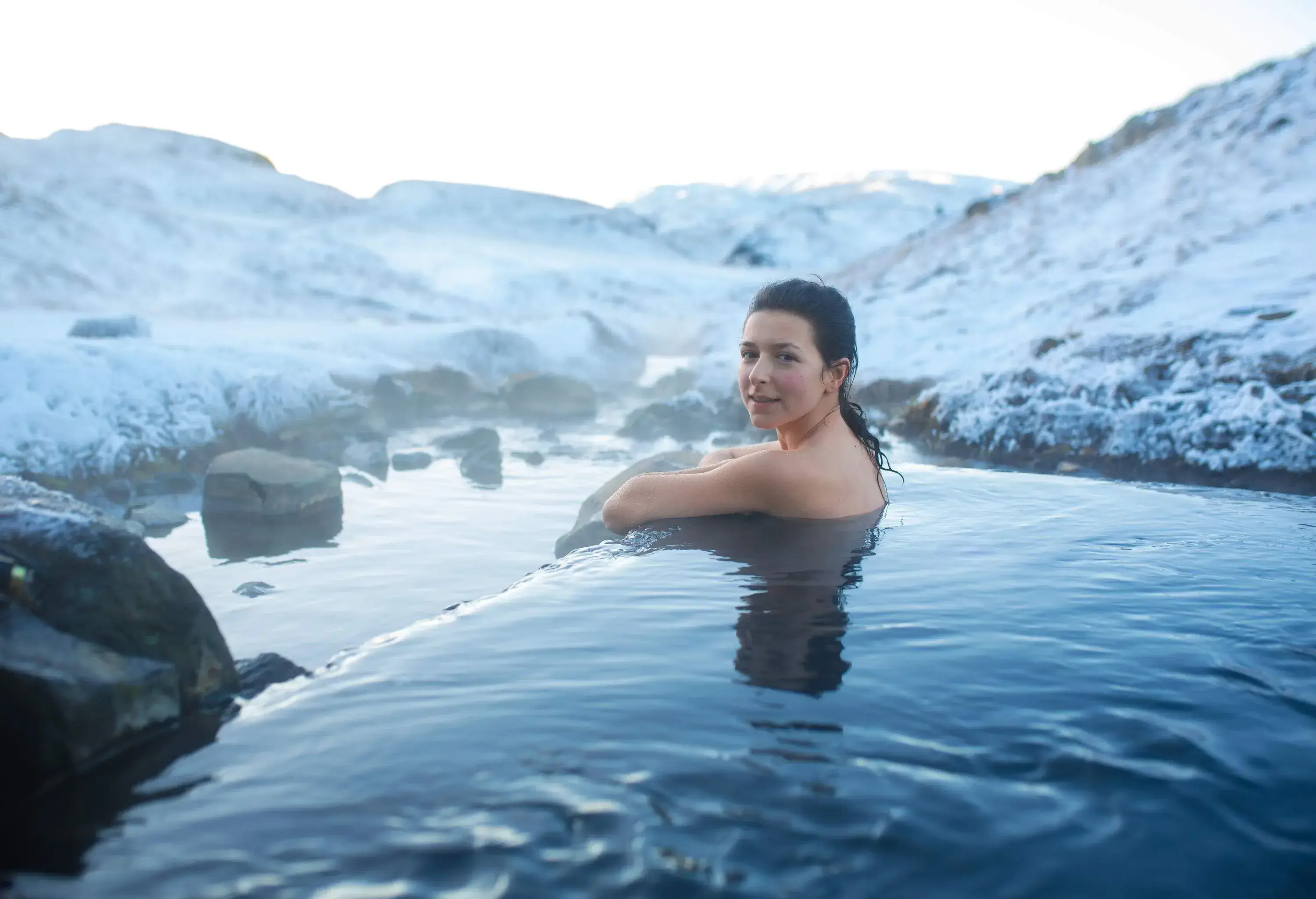The girl bathes in a hot spring in the open air with a gorgeous view of the snowy mountains. Incredible iceland in winter.