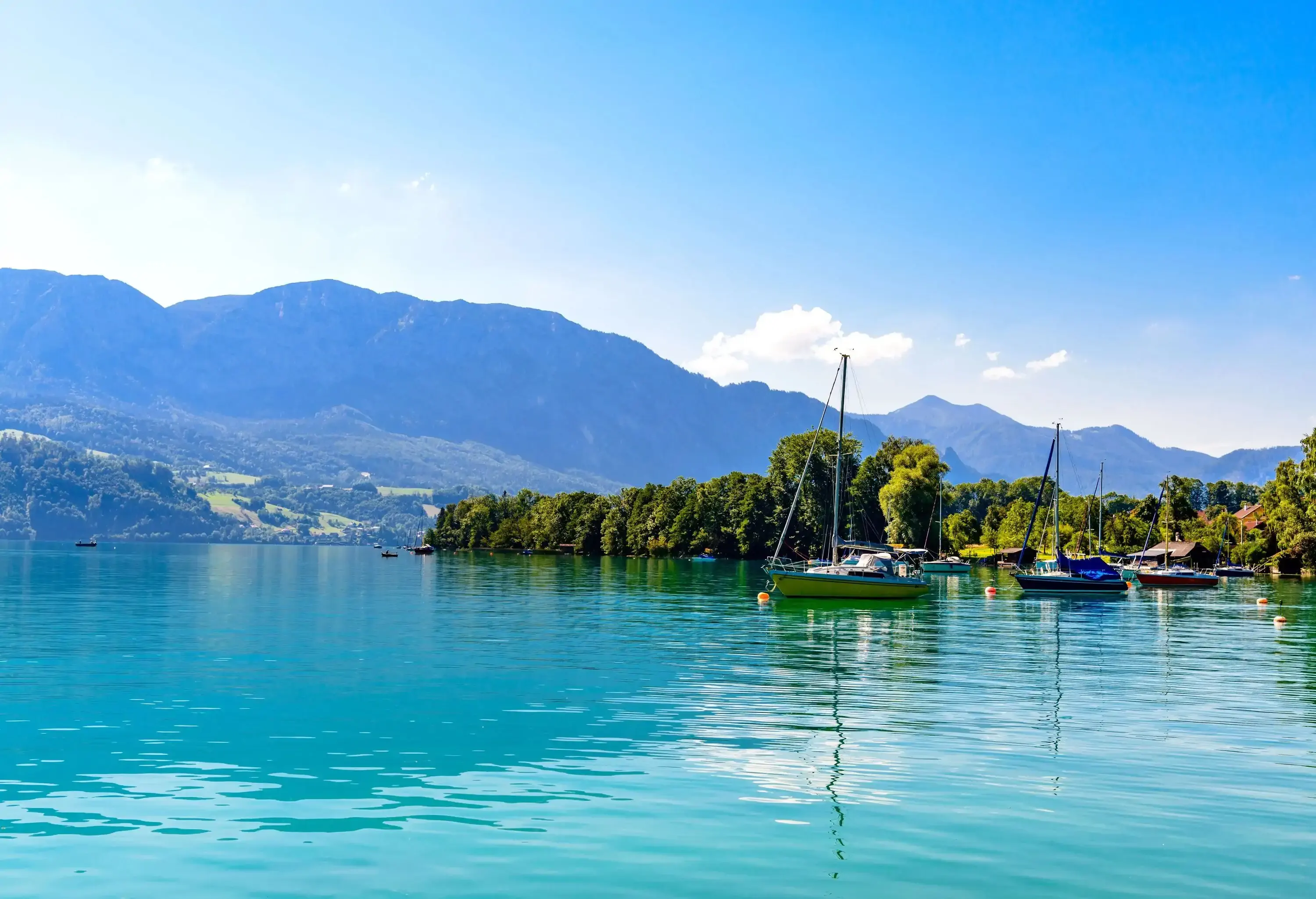 A lovely lake with sailboats floating in the clear water backdropped by the mountains in the distance.