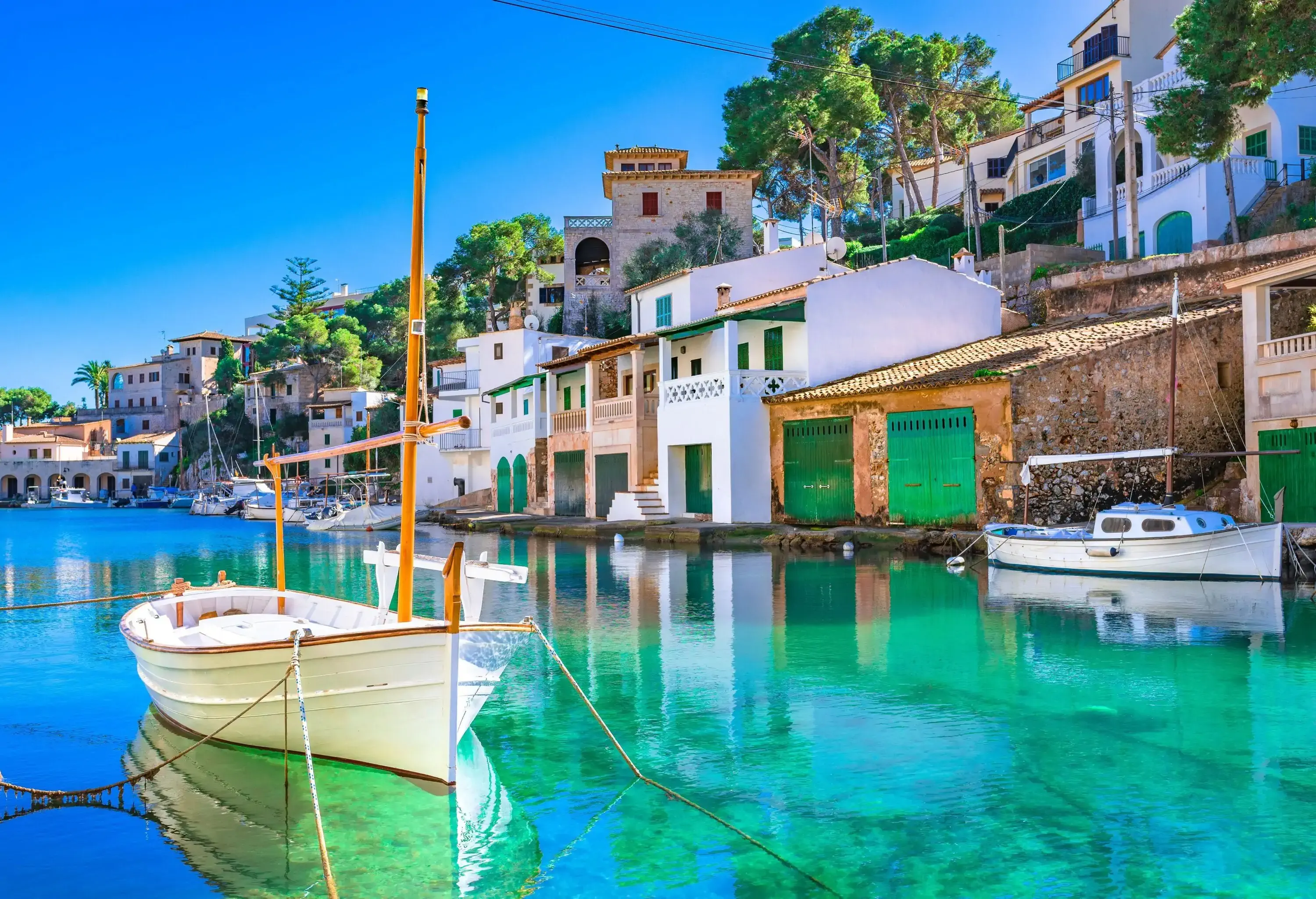 A white boat anchored on a calm harbour with views of waterfront townhouses.