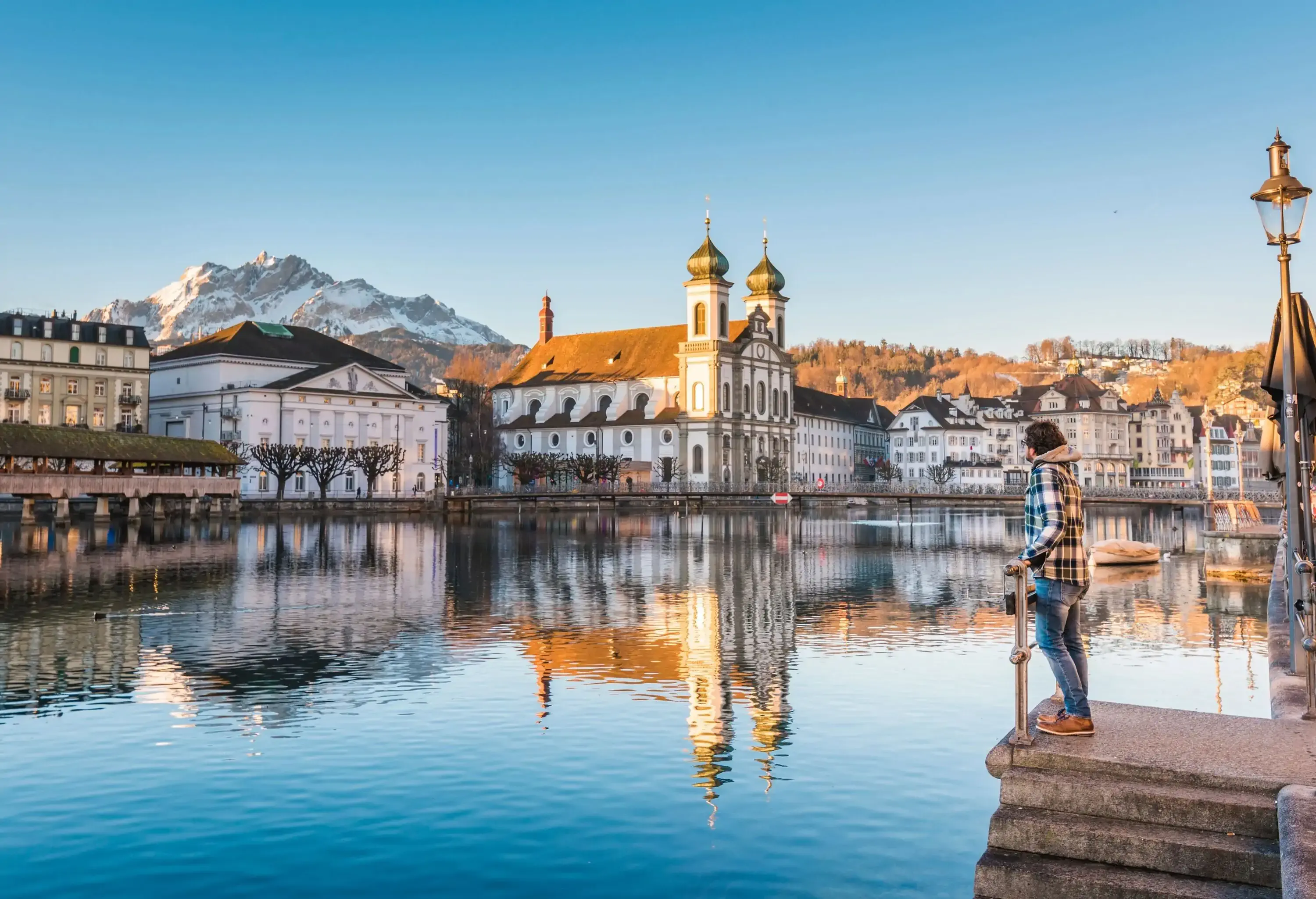 One man looking at the Jesuit Church and Mount Pilatus from the banks of Reuss river in Lucerne, Switzerland