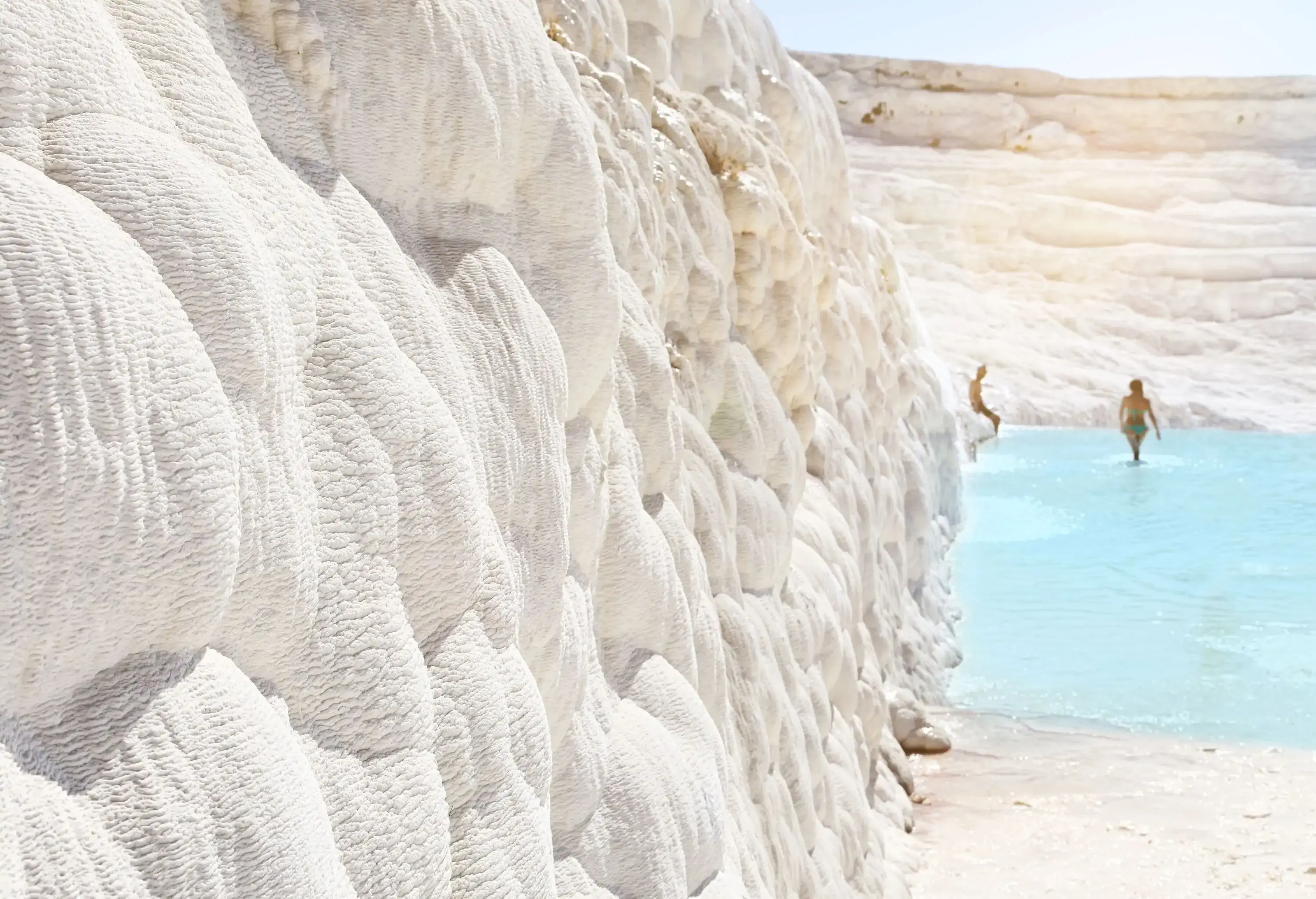 Calcified white rocks in the foreground with an out of focus natural pool and people in the background