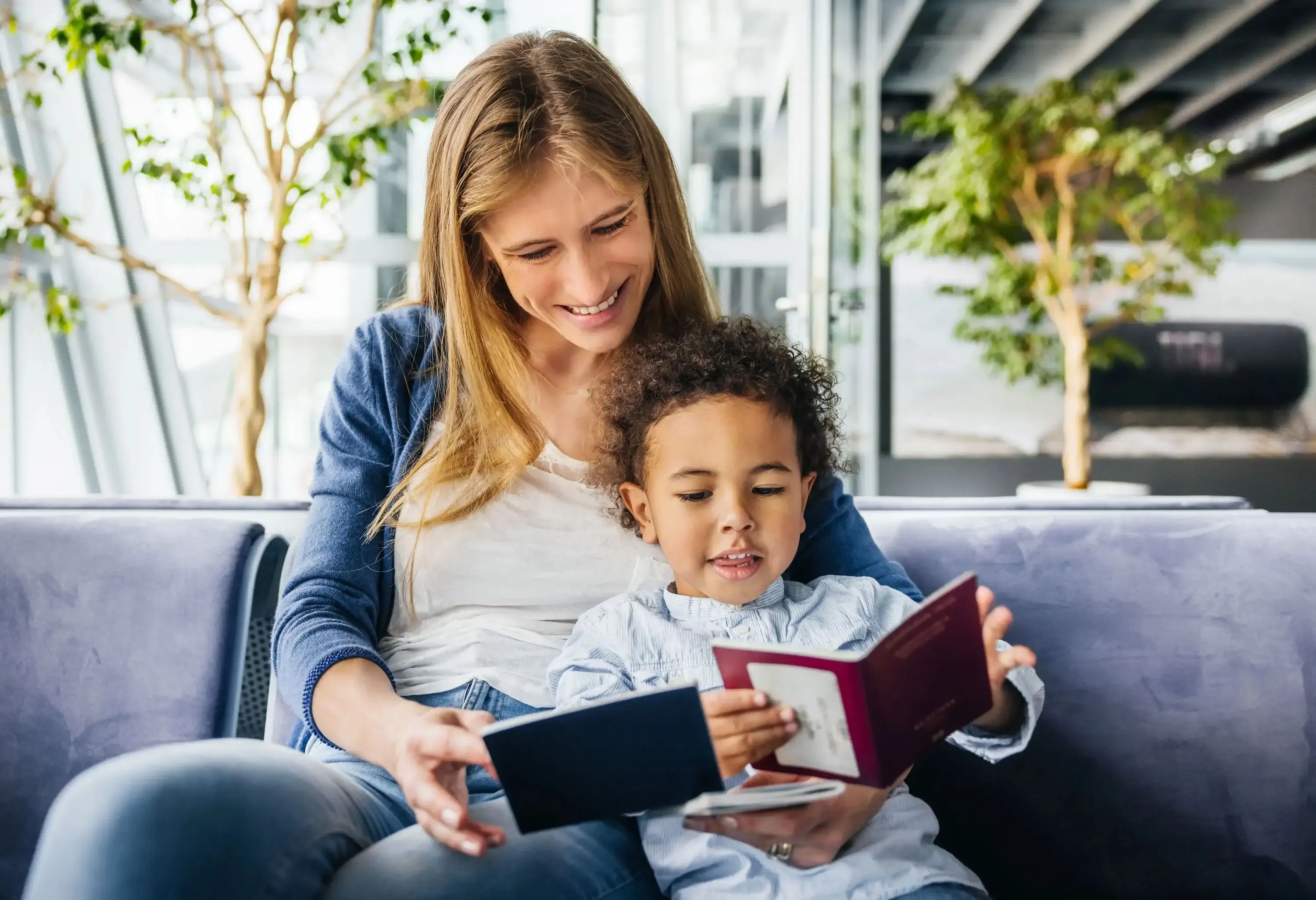 A smiling woman and a young child enjoy reading a book together while waiting in an airport lounge, sharing a moment of happiness together before the flight.