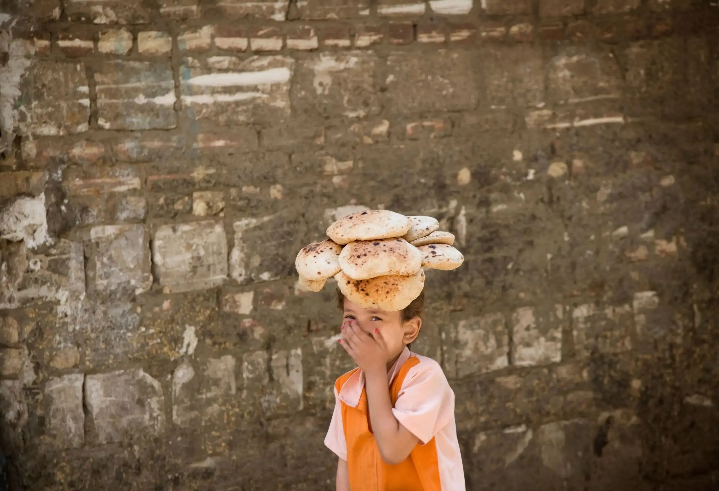 Child laughing and covering mouth carrying bread on his head