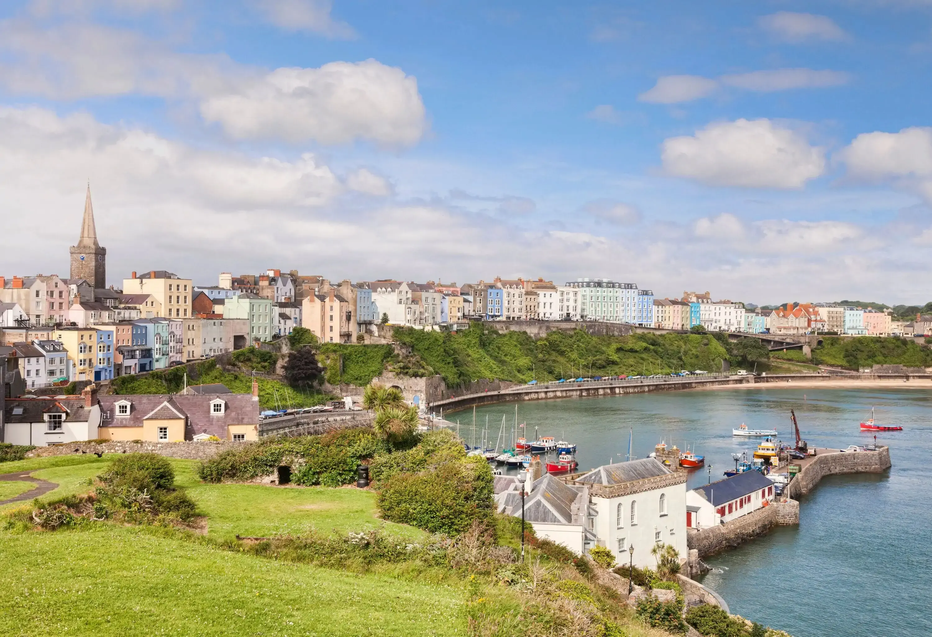 A walled harbour town with a concrete pier surrounded by colourful buildings.