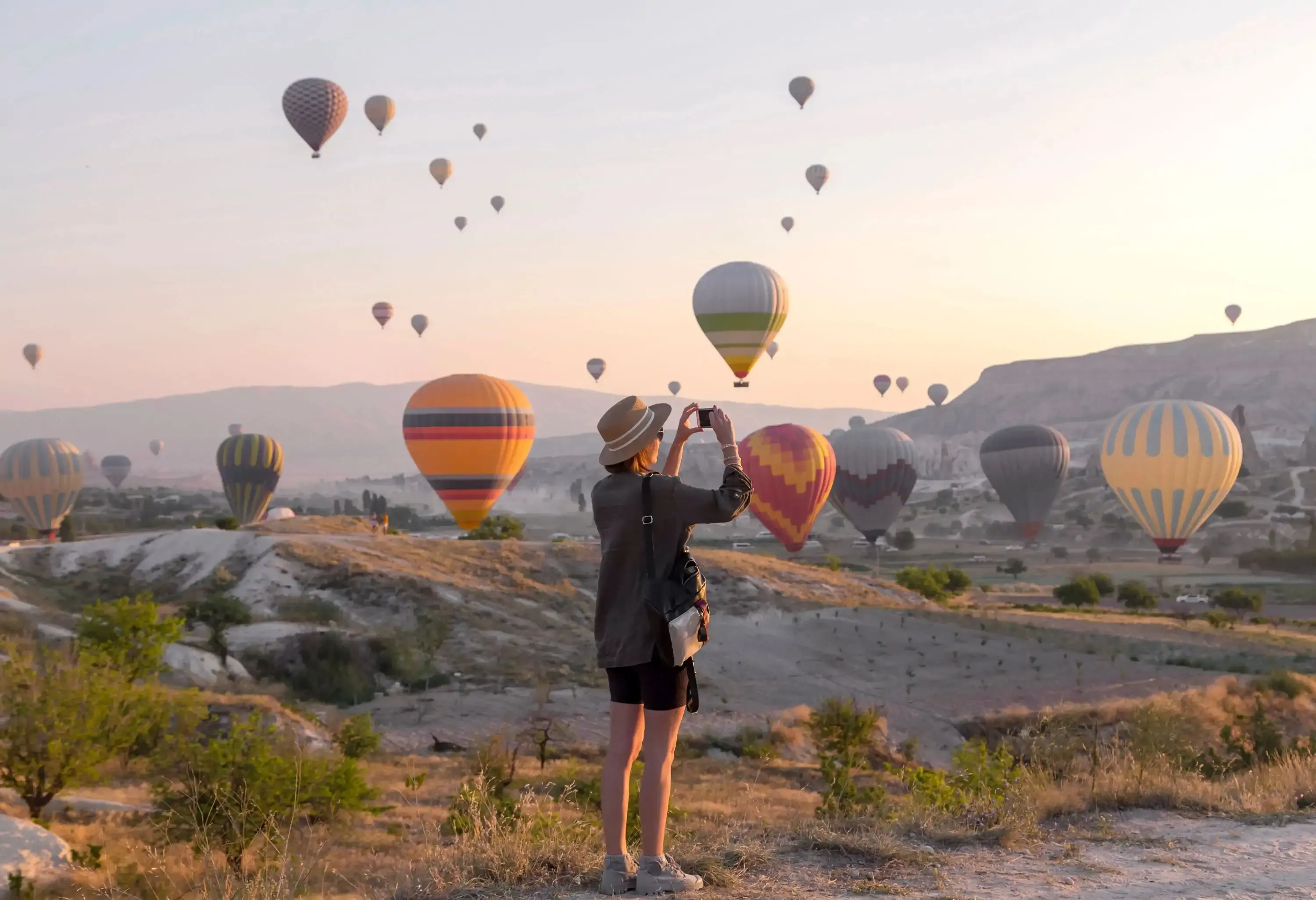 Young woman photographing hot air ballons, Goreme, Cappadocia, Turkey
