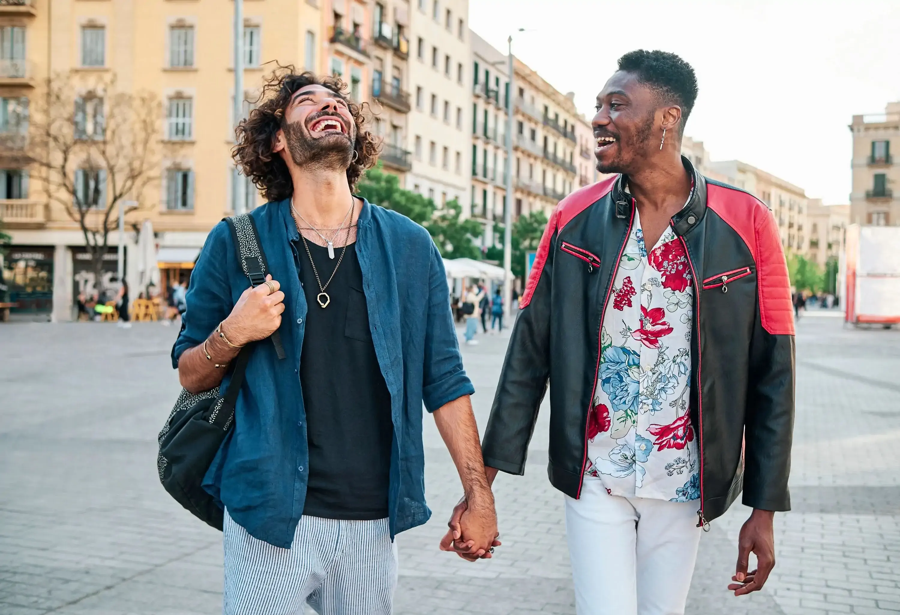 Male couple in casual clothes held hands while laughing, with one looking upwards.