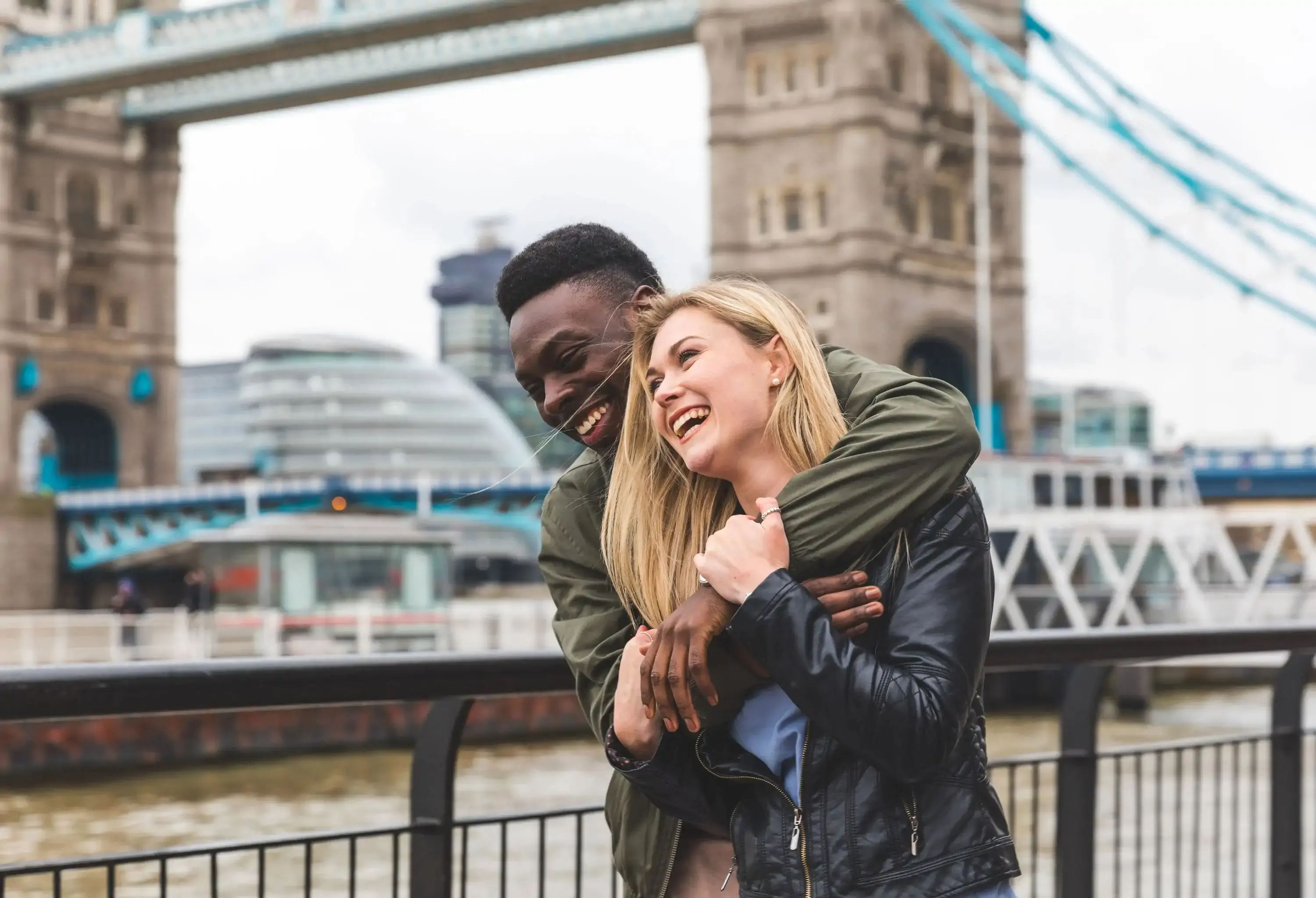 Happy multiracial couple in love in London. Black man and white woman embracing and laughing, bonding and having fun together with Tower Bridge on background.