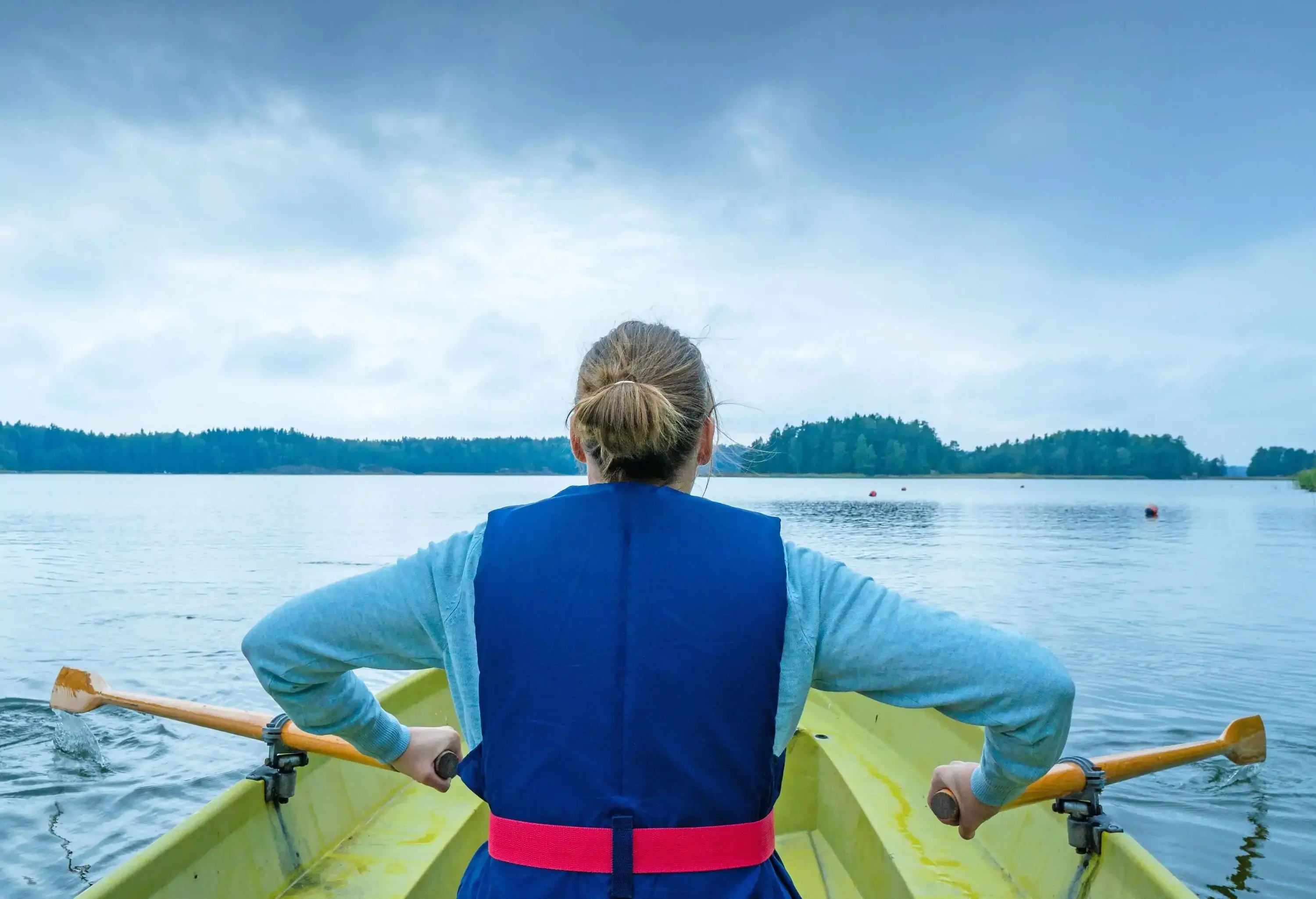 A woman in a row boat over the tranquil sea surrounded by lush islands.