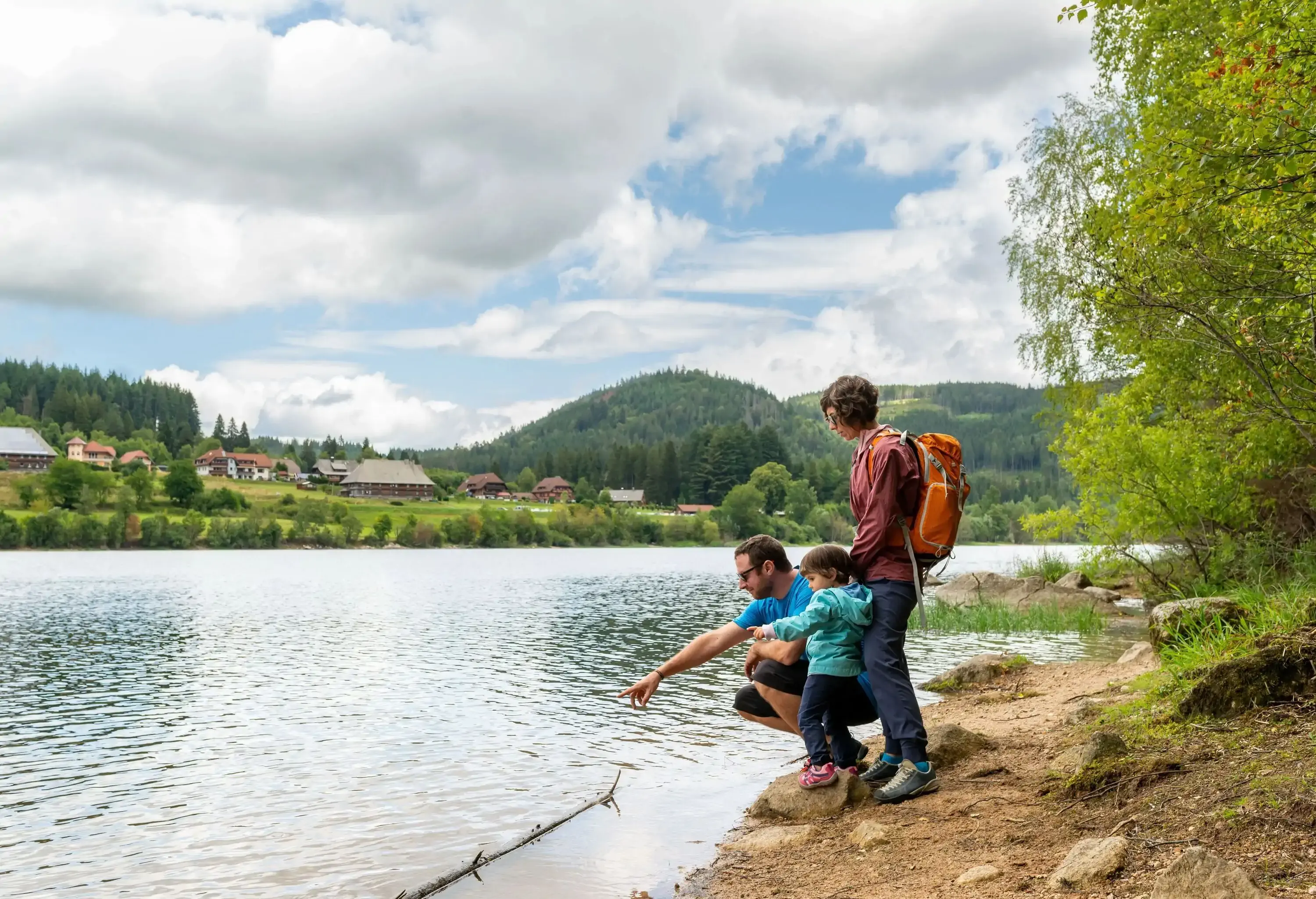 Family enjoyment a day out around Schluchsee in Black Forest, Germany. Father showing something into the water's lake to his little daughter and wife.