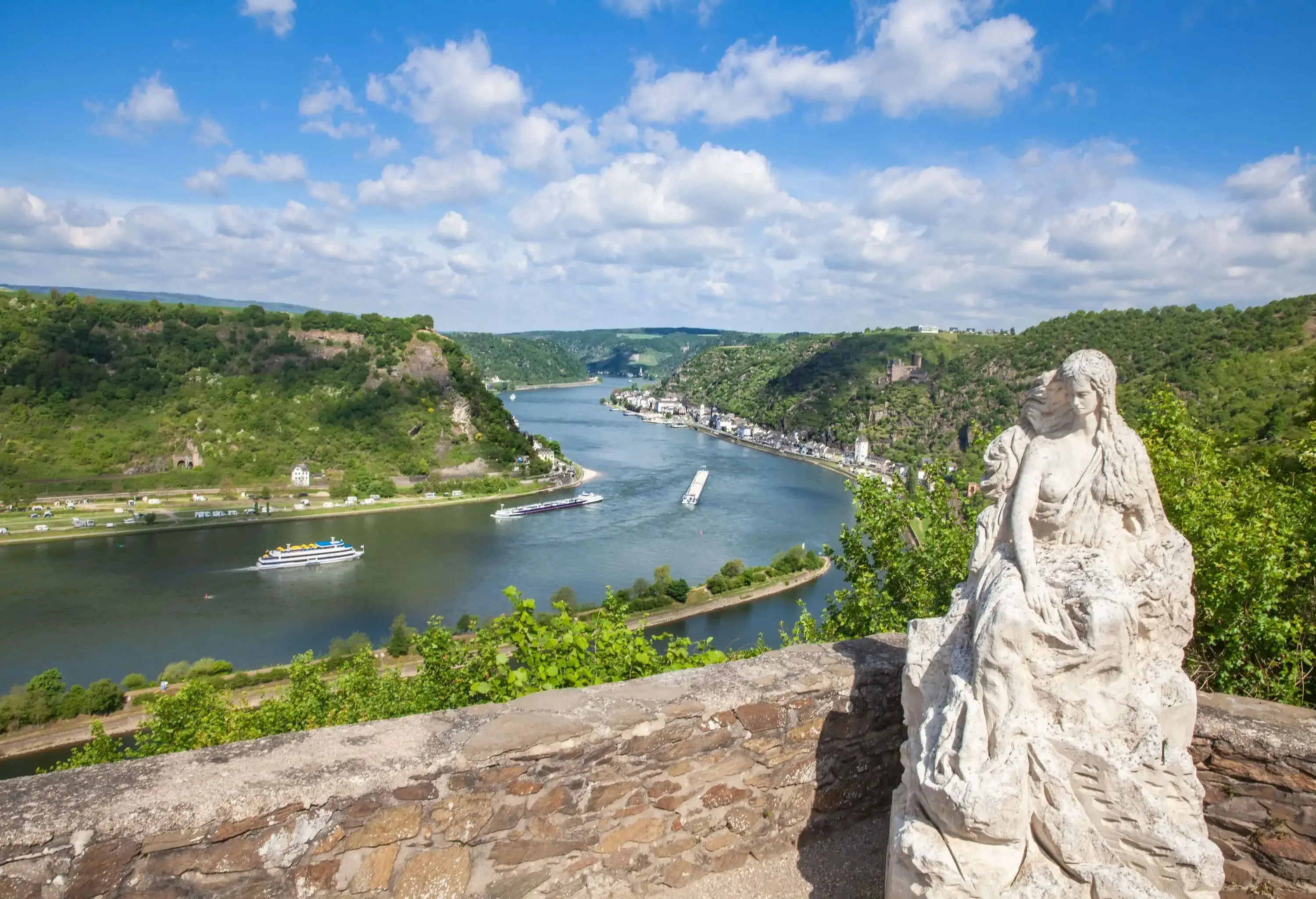 A white sculpture of a woman set on a terrace overlooking a gorge-carved river.
