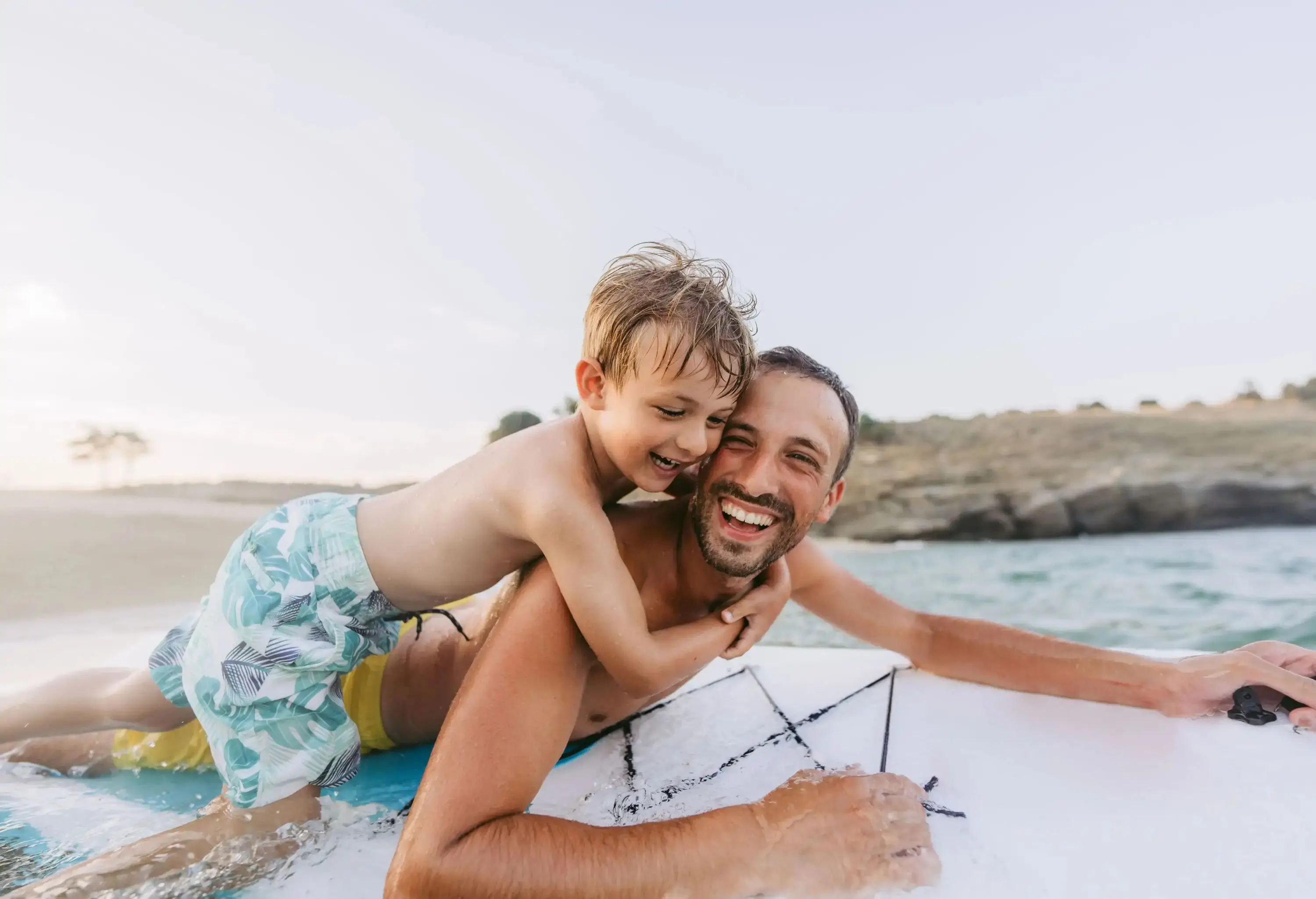 A man lying on a paddleboard in the sea while carrying a little boy on his back.