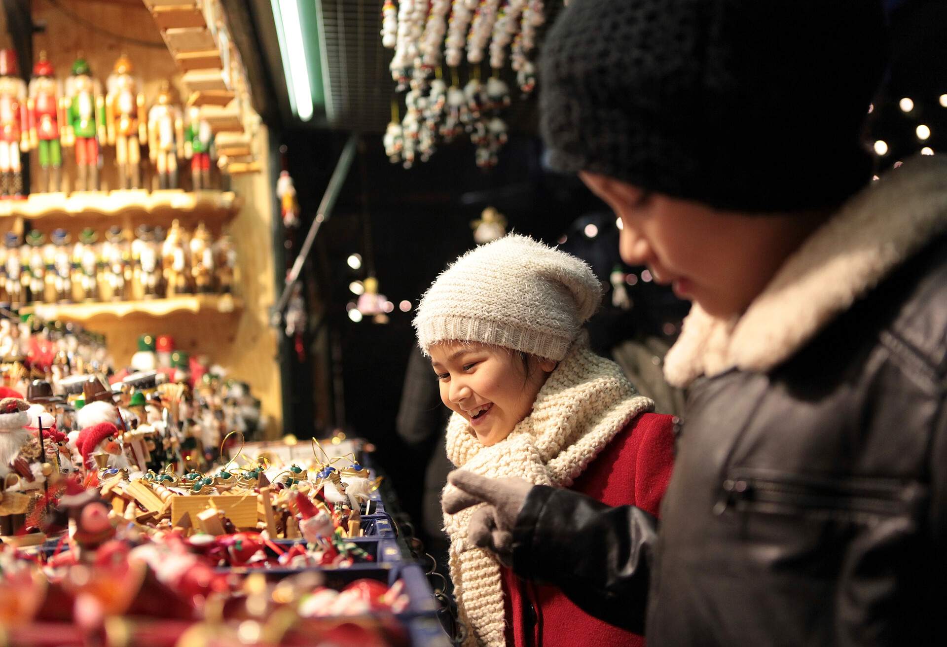 Two children in warm clothing looking at ornaments being sold at a Christmas market.