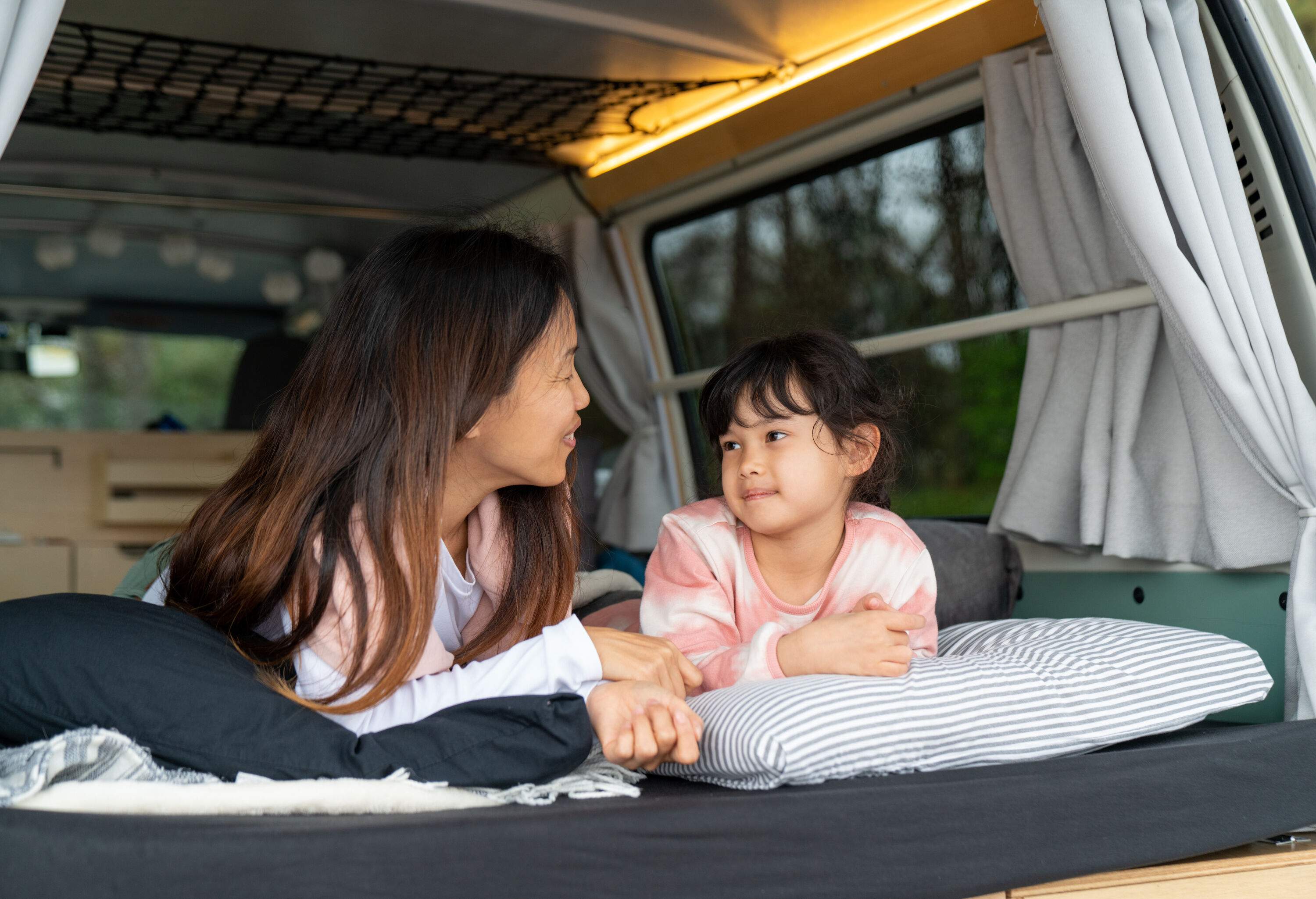 A mother and child laying in bed at the back of an RV looking at each other.