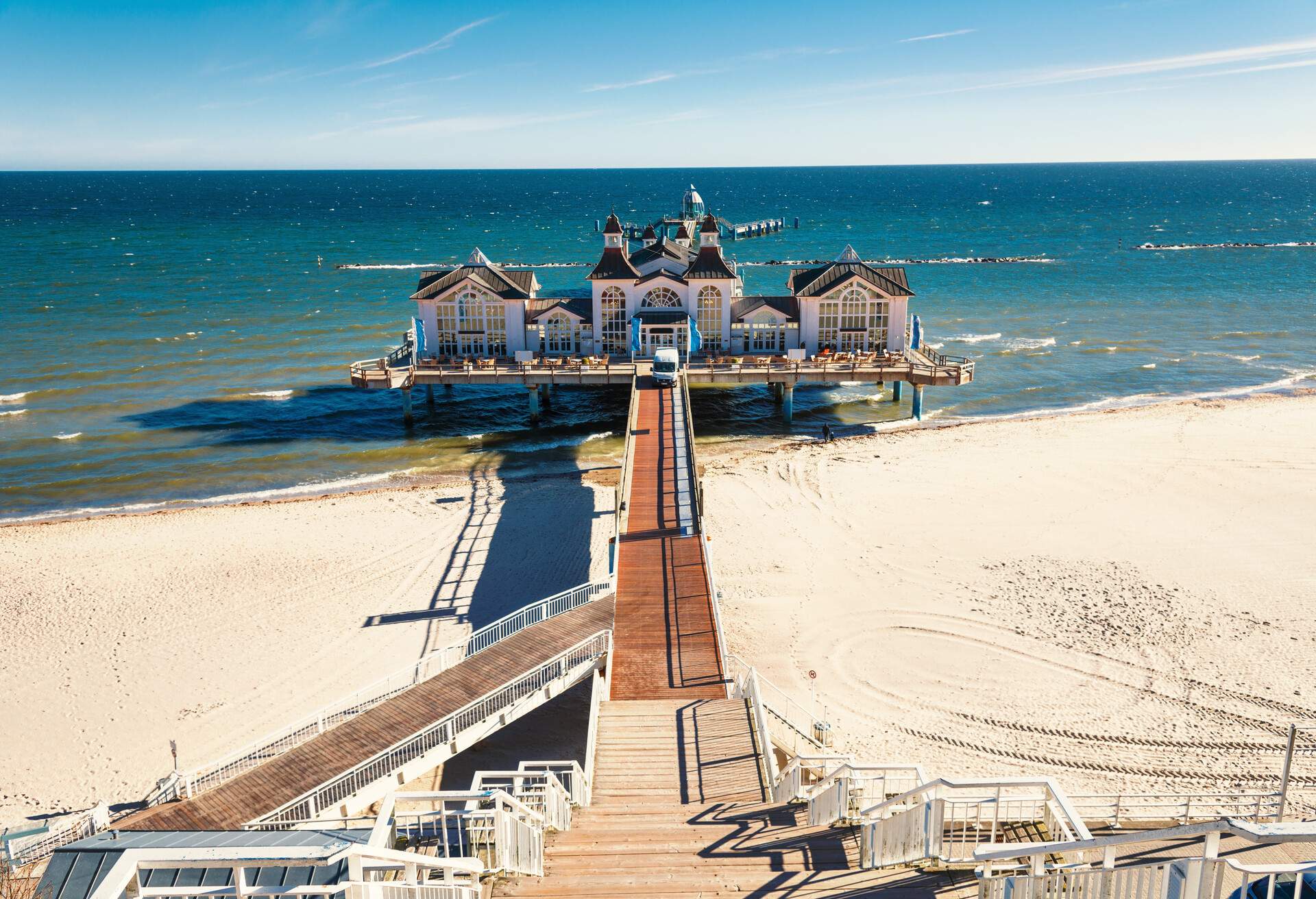 A long promenade leads to a castle-like restaurant on a white-sand beach pier.