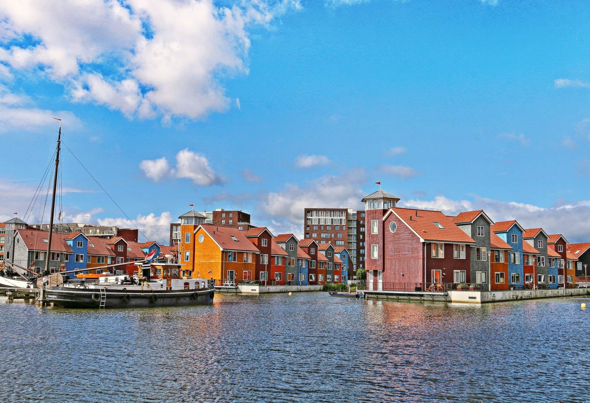 A water canal along a cluster of waterfront colourful apartment buildings and anchored sailboats.